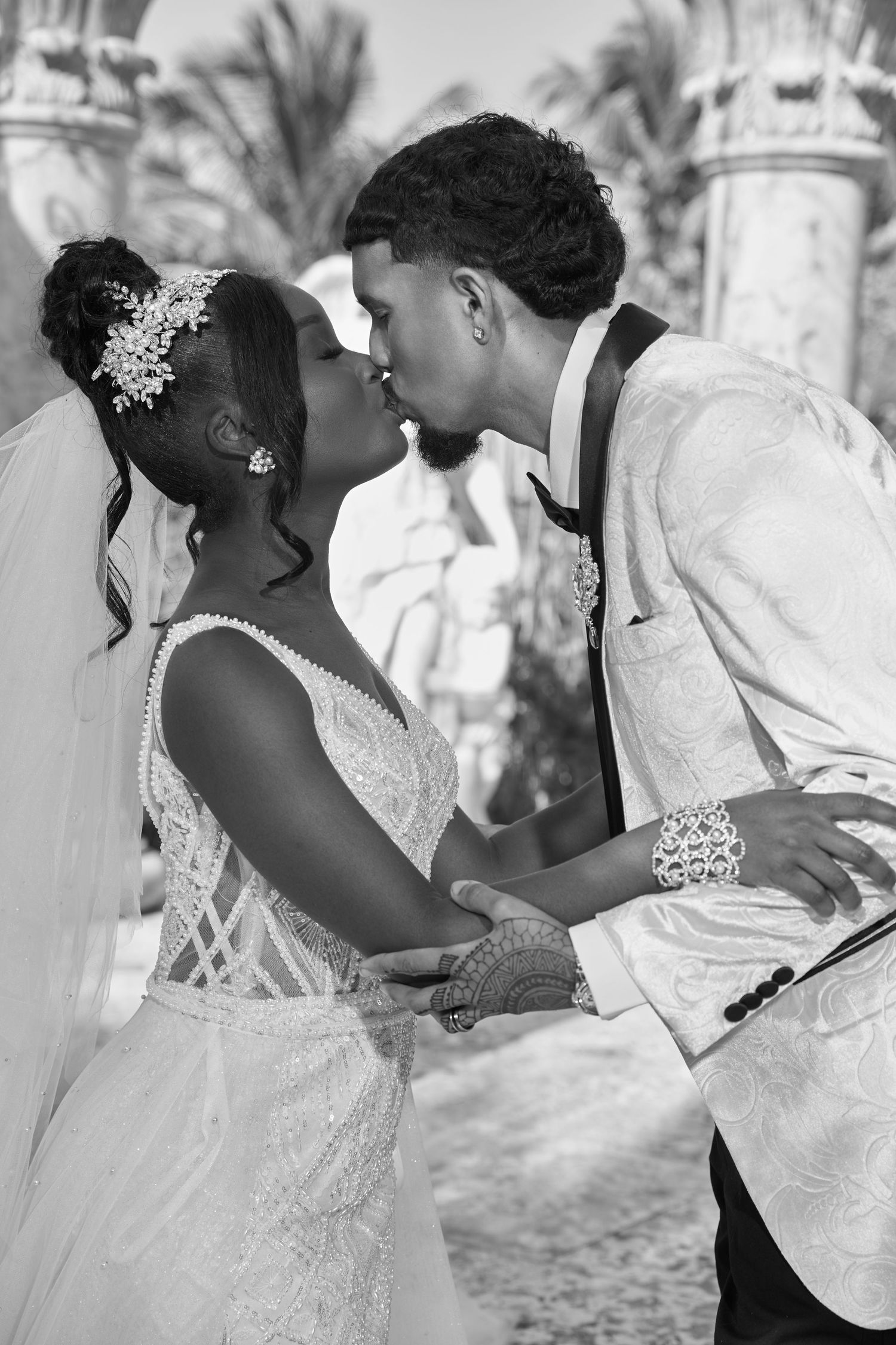 Black and white romantic photo of bride and groom kissing under decorative columns at outdoor ceremony.