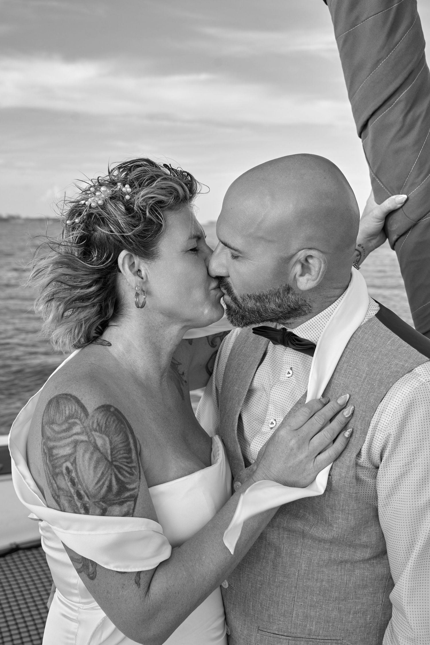 Black and white photo of tattooed bride and bald groom sharing a kiss on a sailboat.