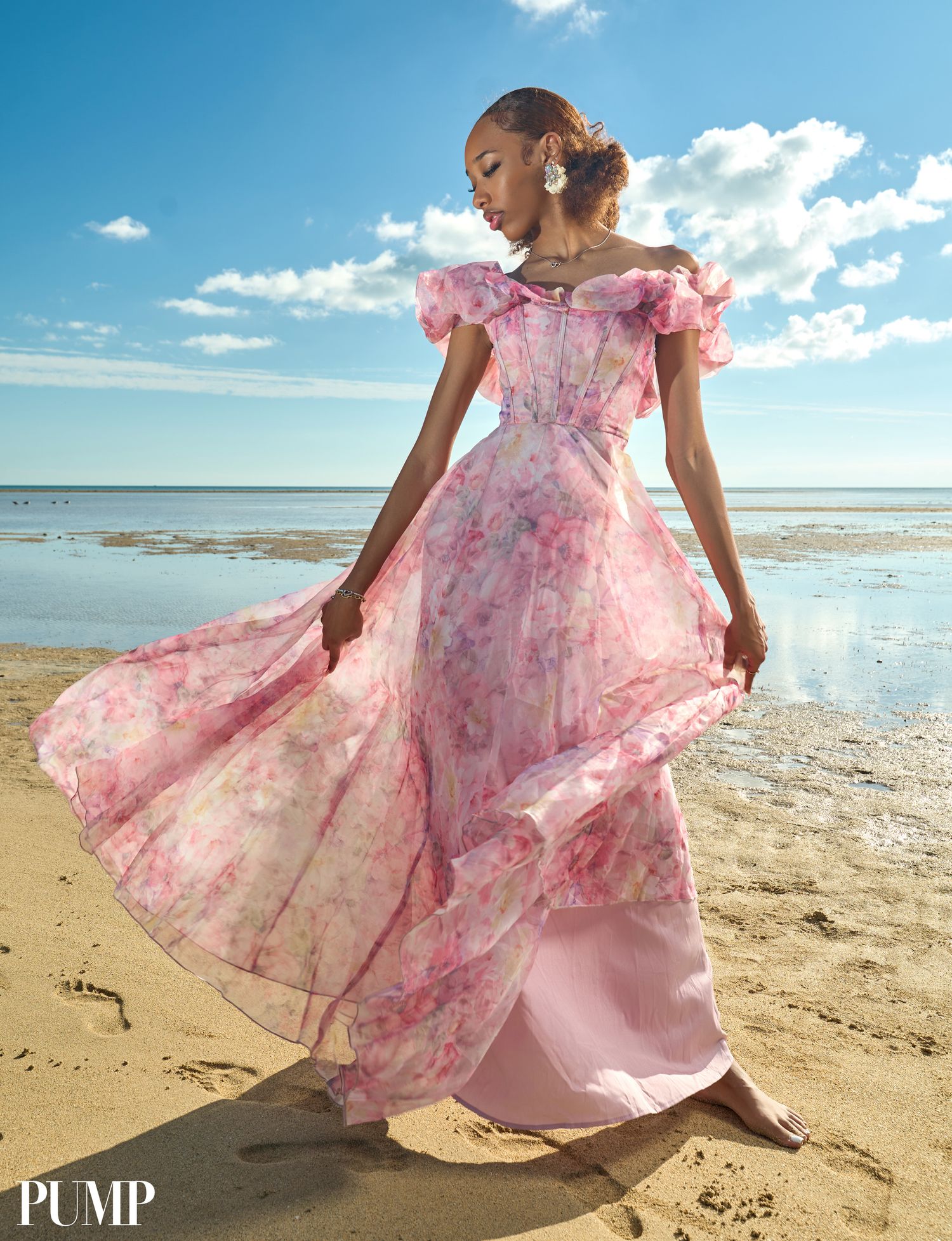 Elegant model stands on beach wearing a romantic pink floral off-shoulder maxi dress with ruffled details.
