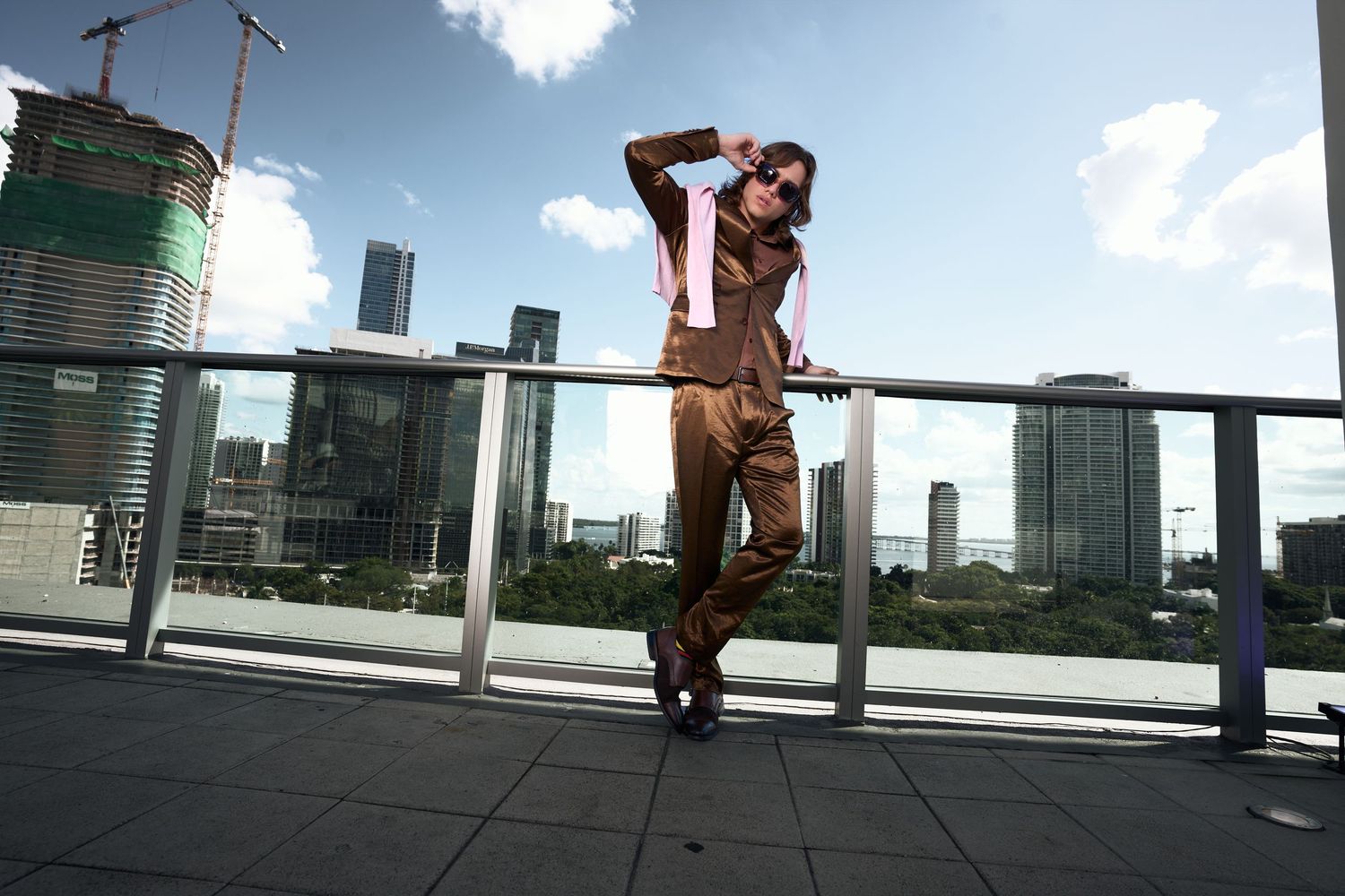Stylish woman in brown pantsuit posing on urban rooftop terrace with city skyline backdrop.