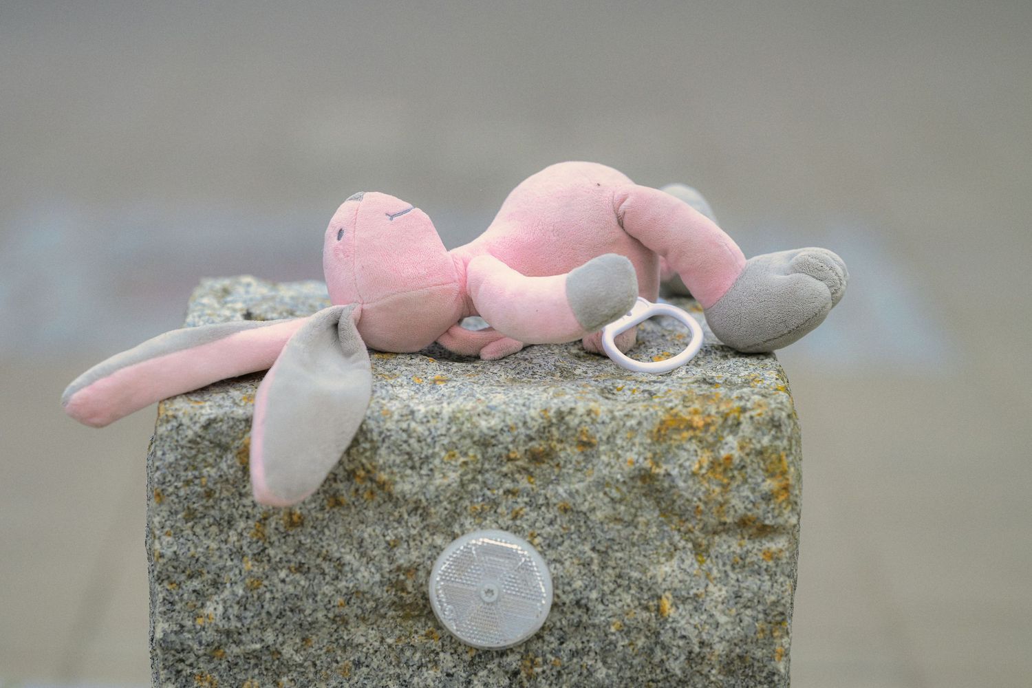 Pink plush bunny toy with pacifier resting on gray stone surface outdoors.