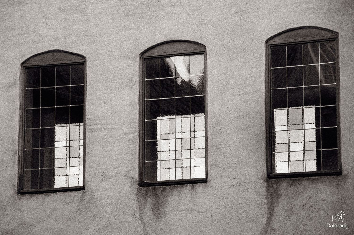 Row of arched windows along an industrial building's concrete wall creates a repeating architectural pattern in black and white.