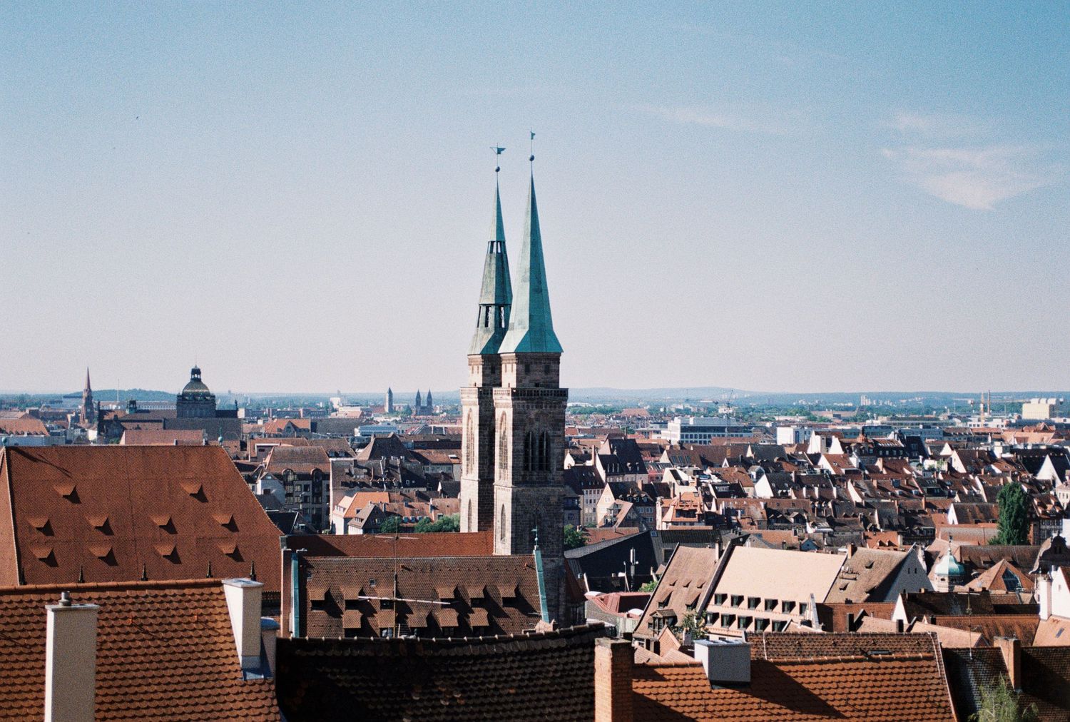 Panoramic cityscape of Nuremberg showing historic architecture, church spires, and red-tiled rooftops under blue sky.