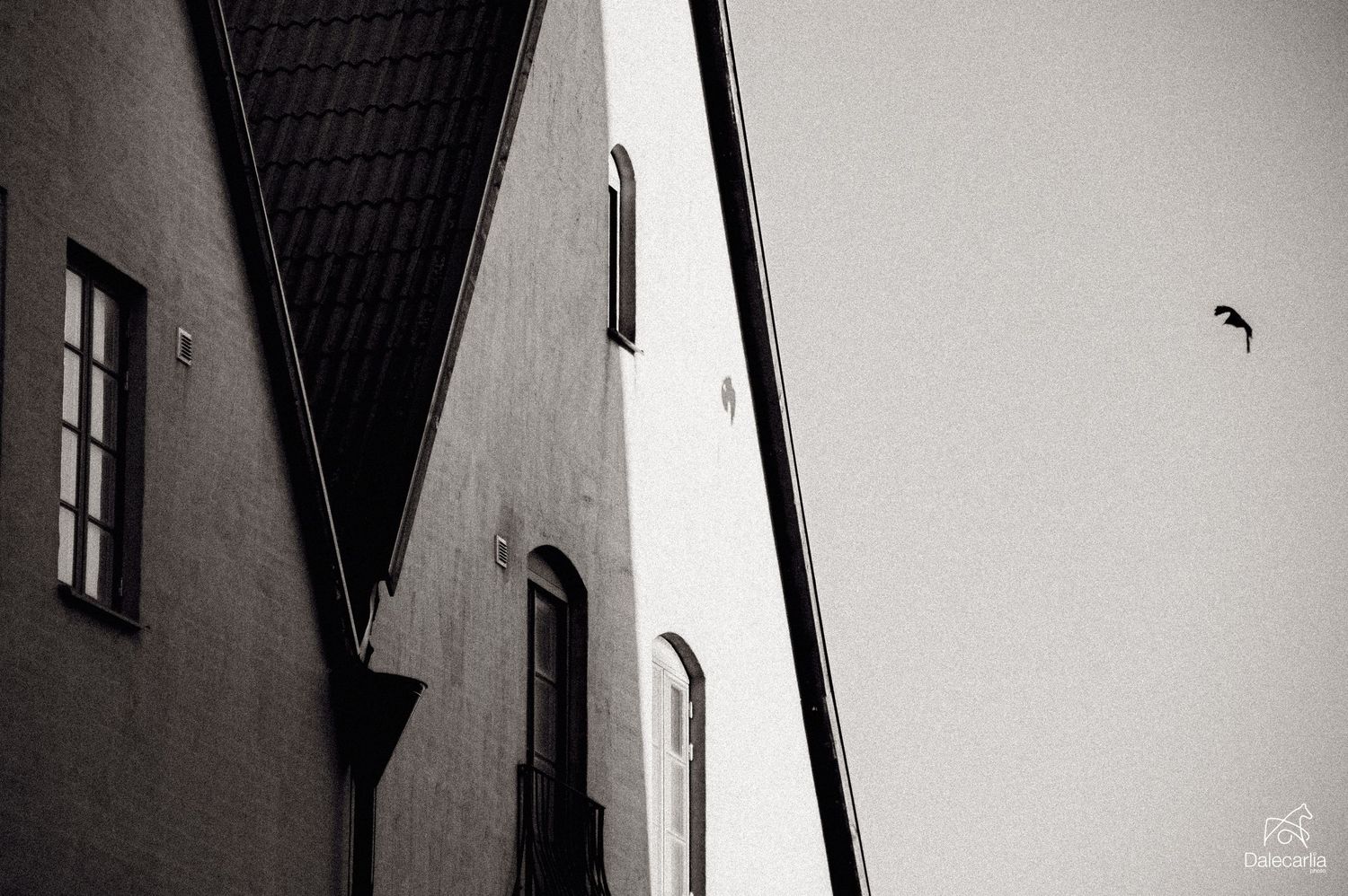 Black and white architectural photo showing a dark window against a white building facade with dramatic shadows.
