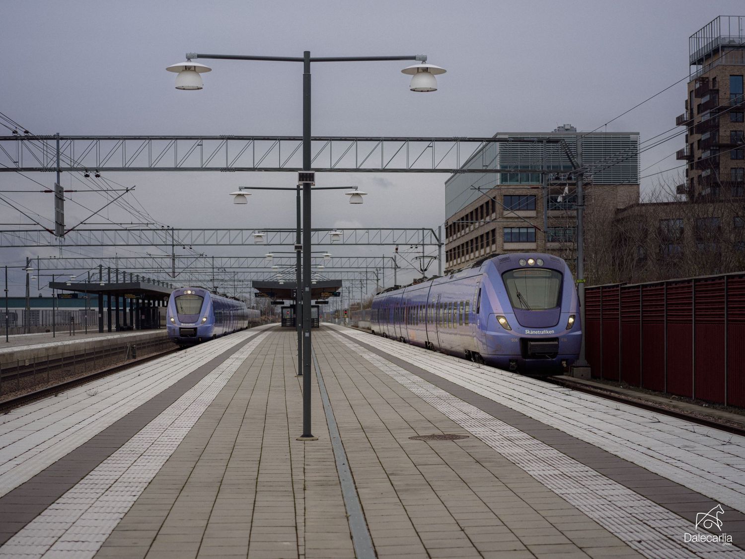A series of empty train platforms at a transit station with overhead power lines and modern infrastructure.