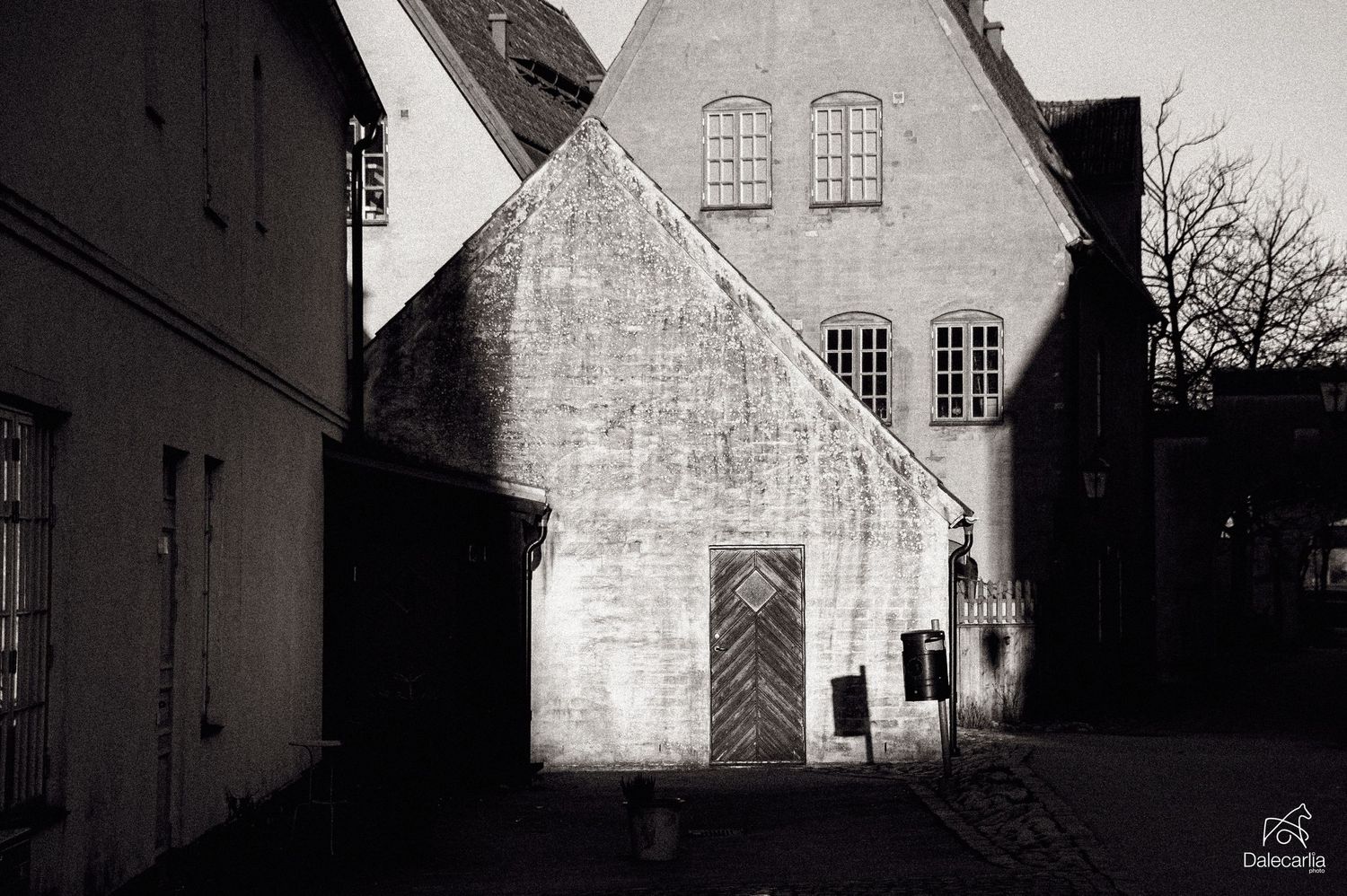 Black and white photograph of a historic stone building with arched doorway and windows casting shadows in an old town street.