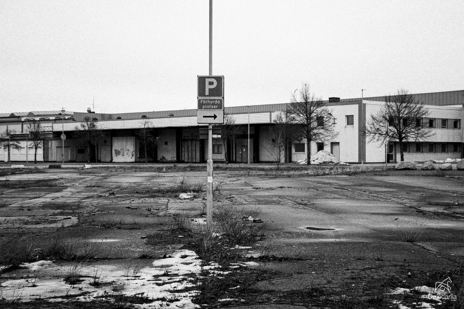 A black and white aerial view shows an abandoned strip mall with empty parking lots and deteriorating buildings.