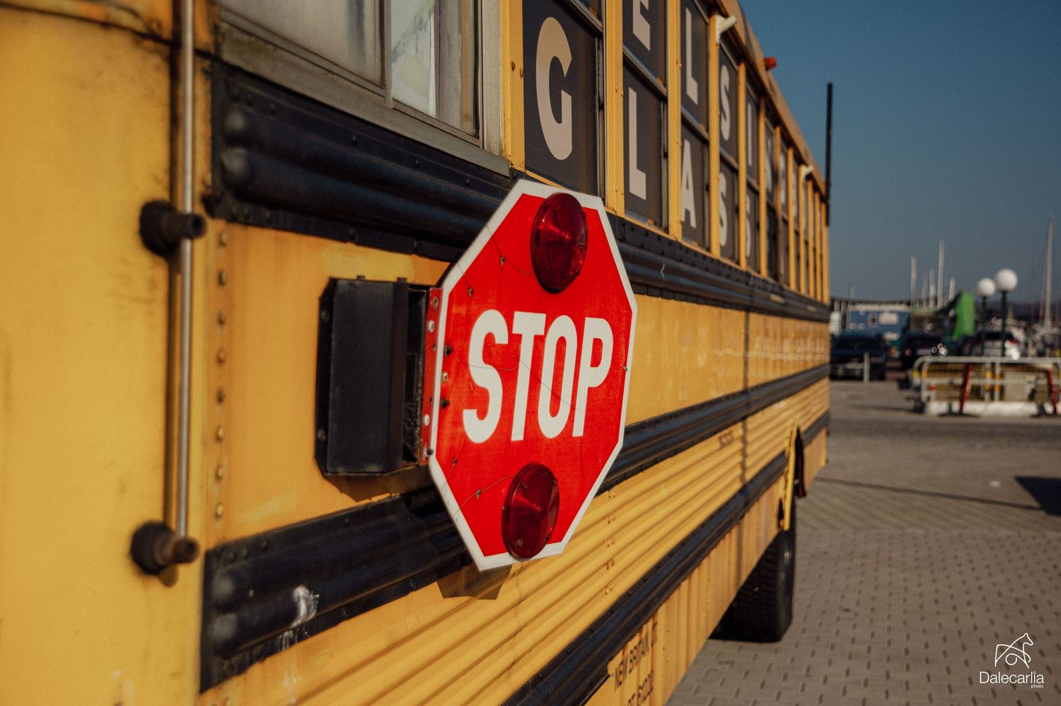 Yellow school bus with a red stop sign on the side, parked in a lot on a sunny day.