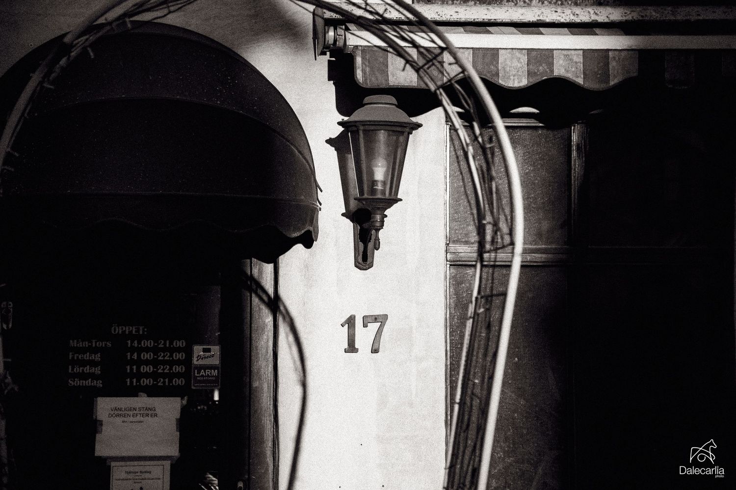Monochromatic urban scene featuring arched doorways and lanterns along a building's exterior wall.