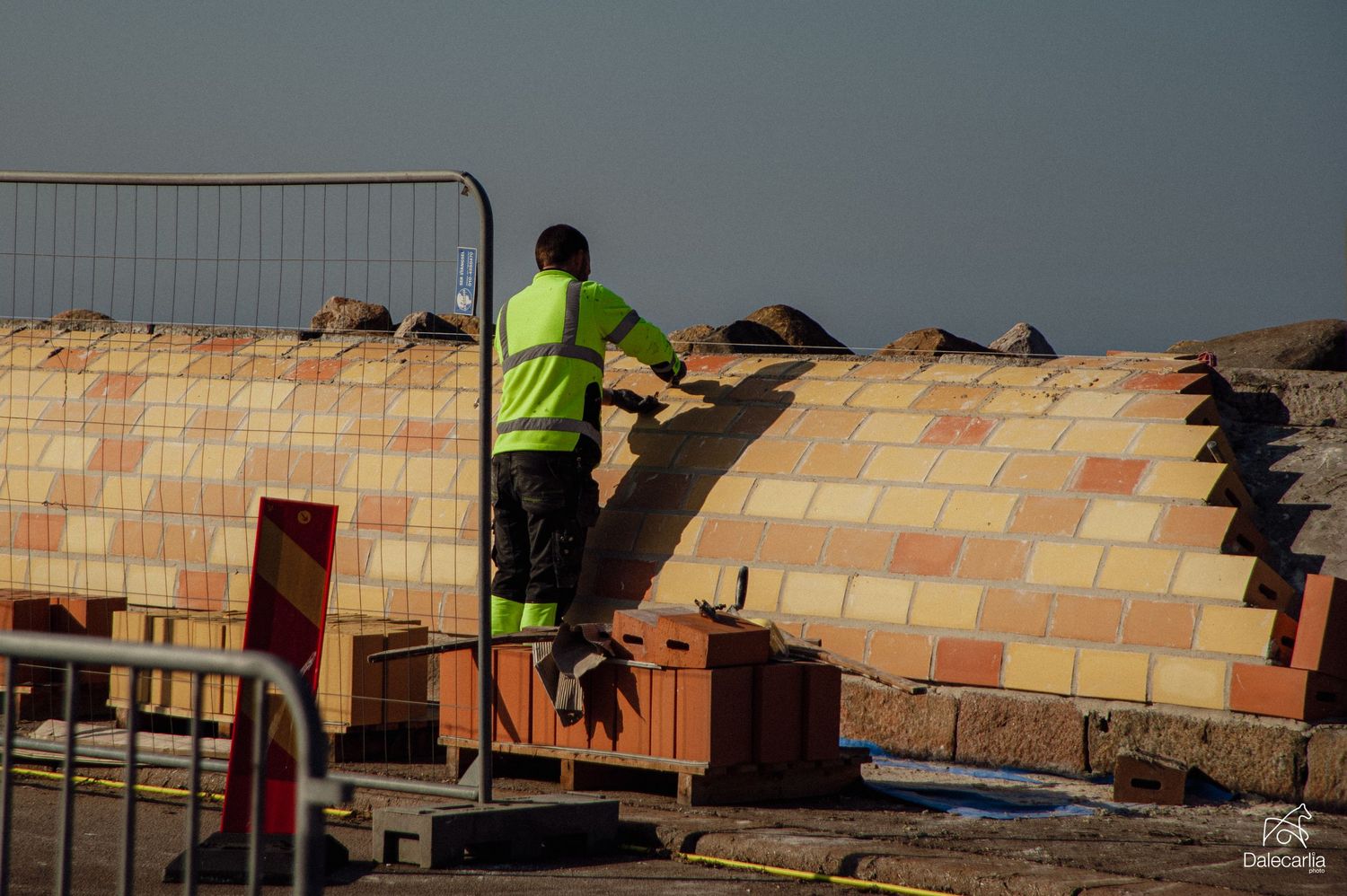 Construction worker in high-visibility vest building a colorful brick wall at an outdoor site.