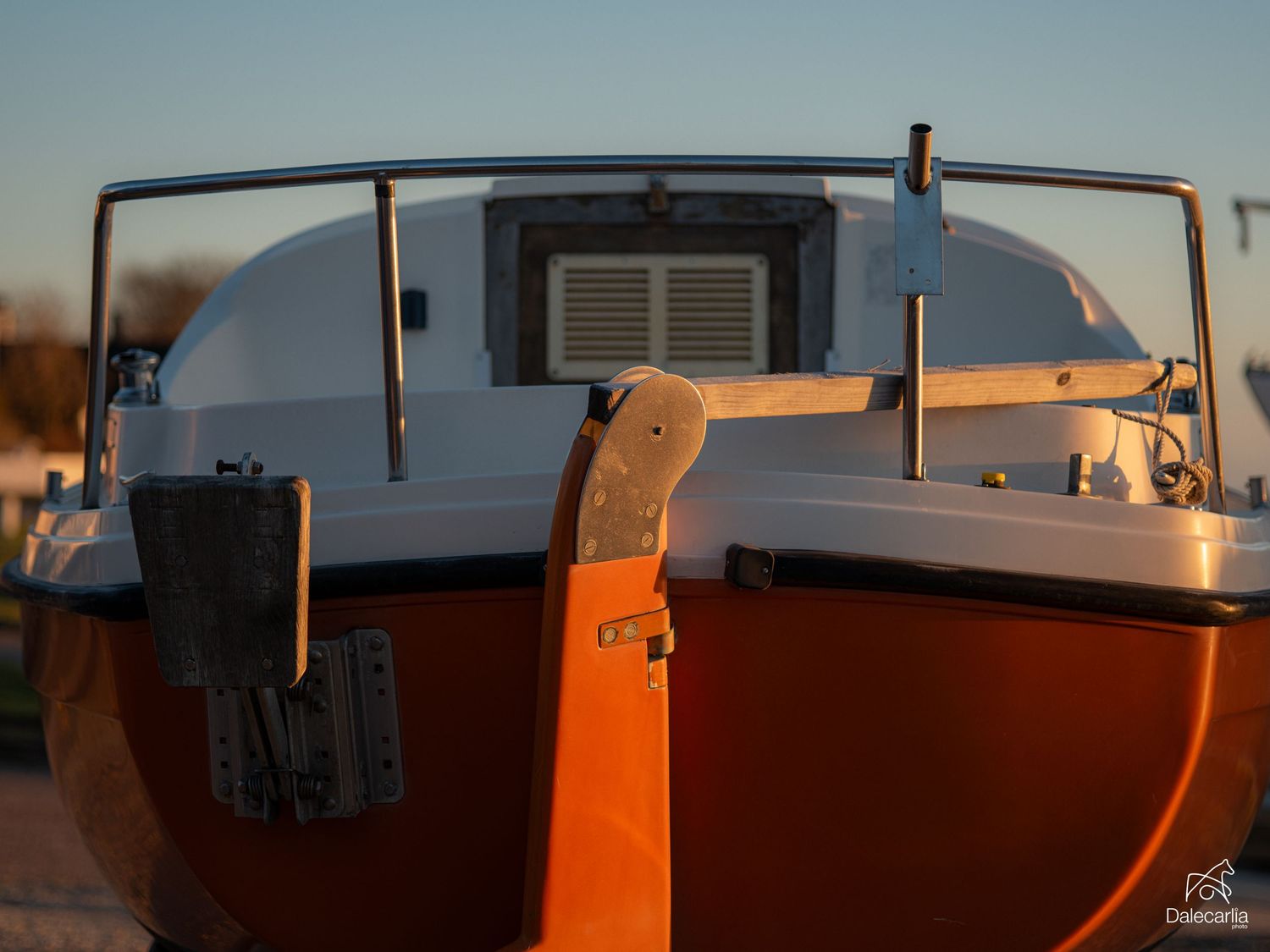 Red and white sailboat stern with metal railings and ventilation grille photographed in warm golden hour sunlight.
