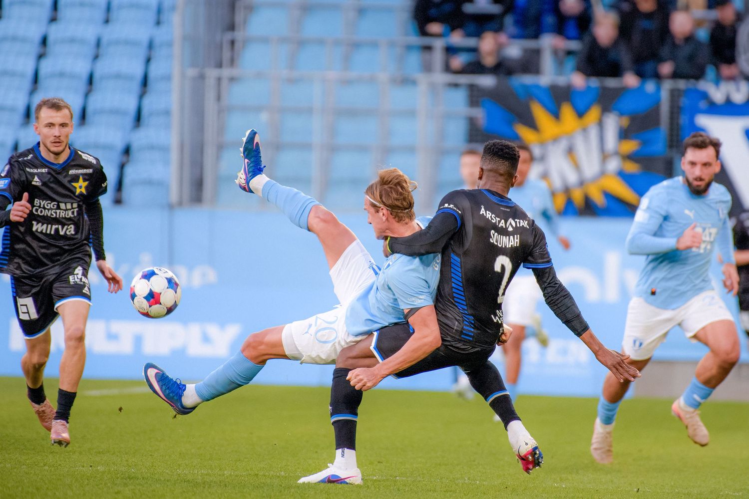 Two soccer players compete for the ball during an intense match, with one player performing a dramatic kick on the field.