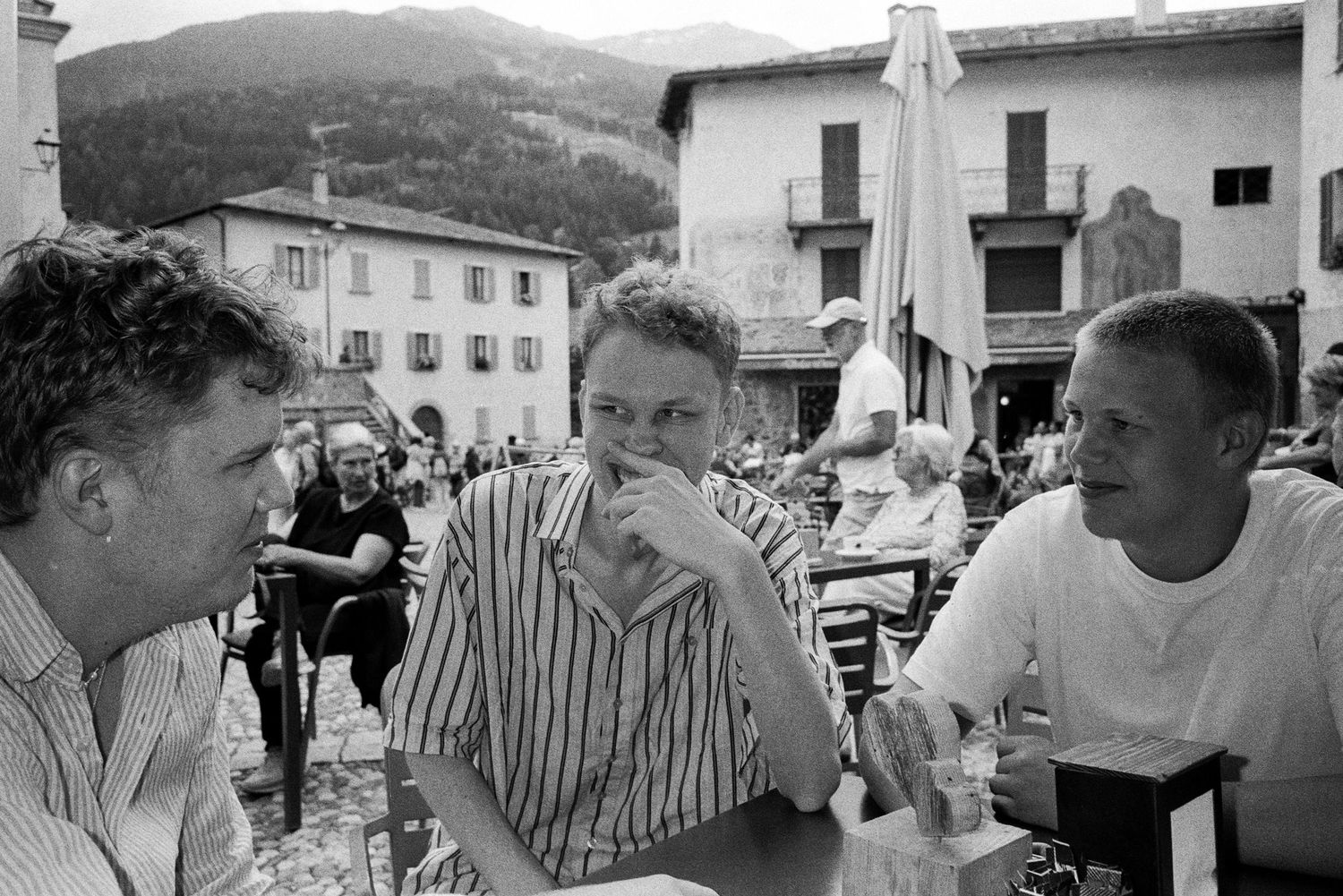 A black and white photograph shows three people sitting at an outdoor cafe in Europe.
