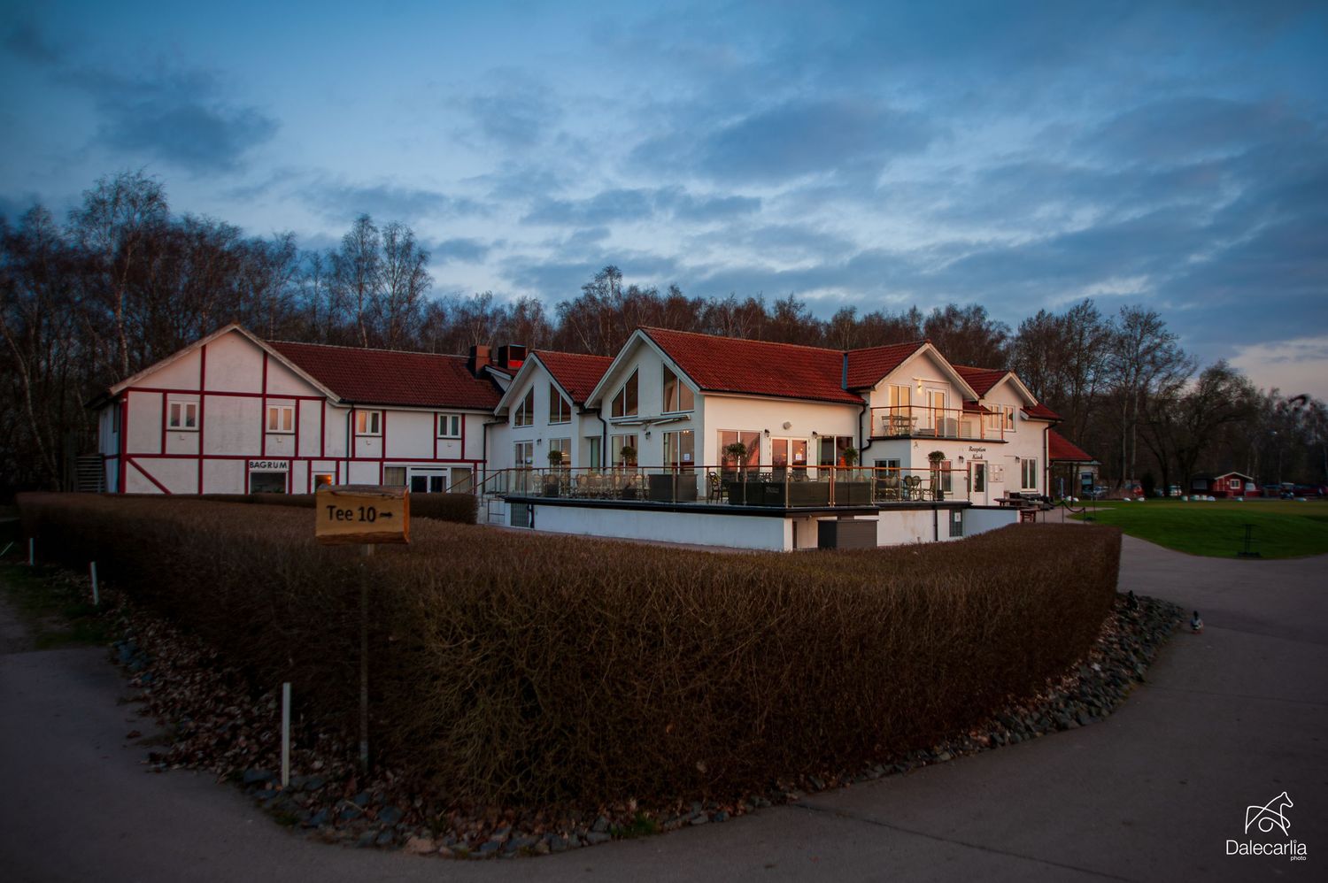 A charming European hotel complex with white and red buildings nestled among trees at dusk under a dramatic blue sky.