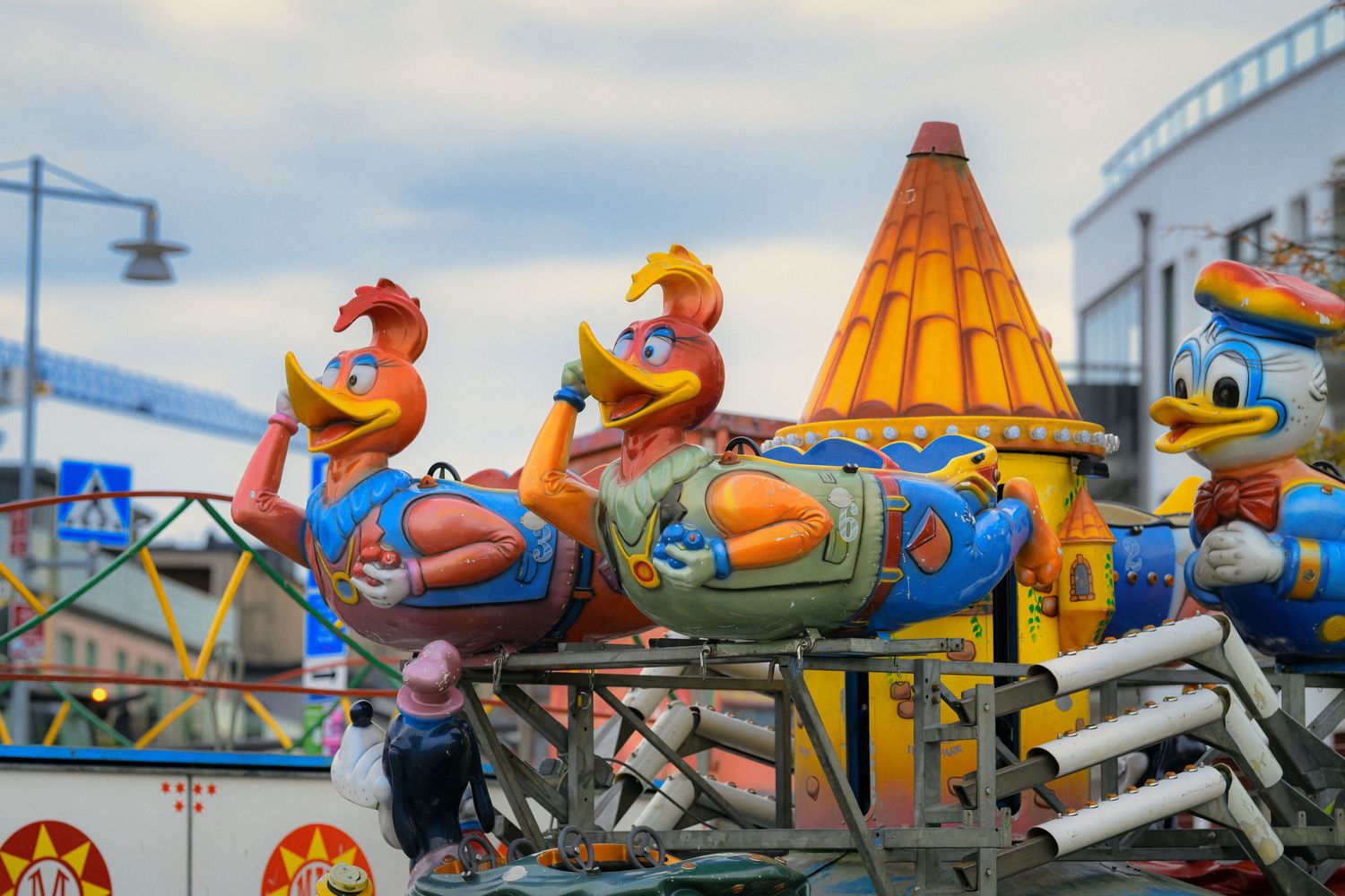 Colorful carnival ride featuring cartoon characters in rocket-shaped vehicles against a cloudy sky at an amusement park.