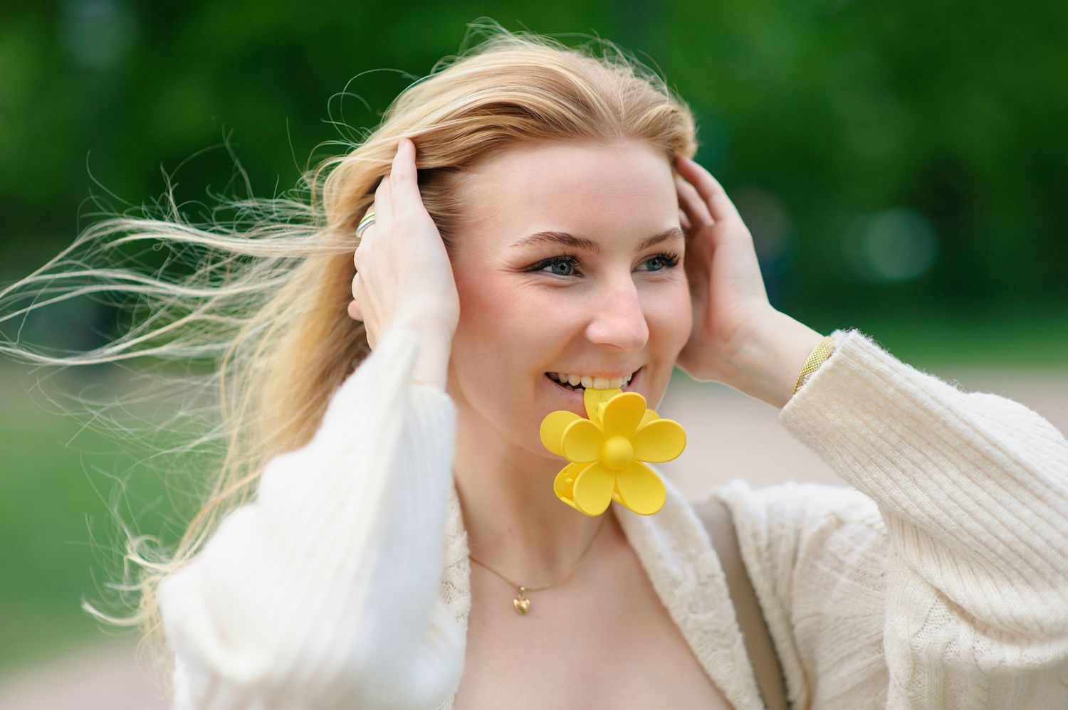 Person holding a cheerful yellow daffodil flower while wearing a cream sweater outdoors on a breezy spring day.