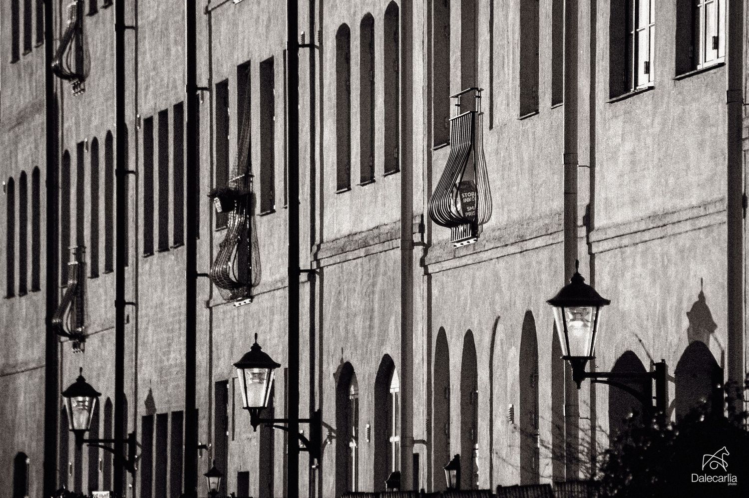 Black and white architectural detail of historic building facade with ornate lanterns and windows creating dramatic shadows.