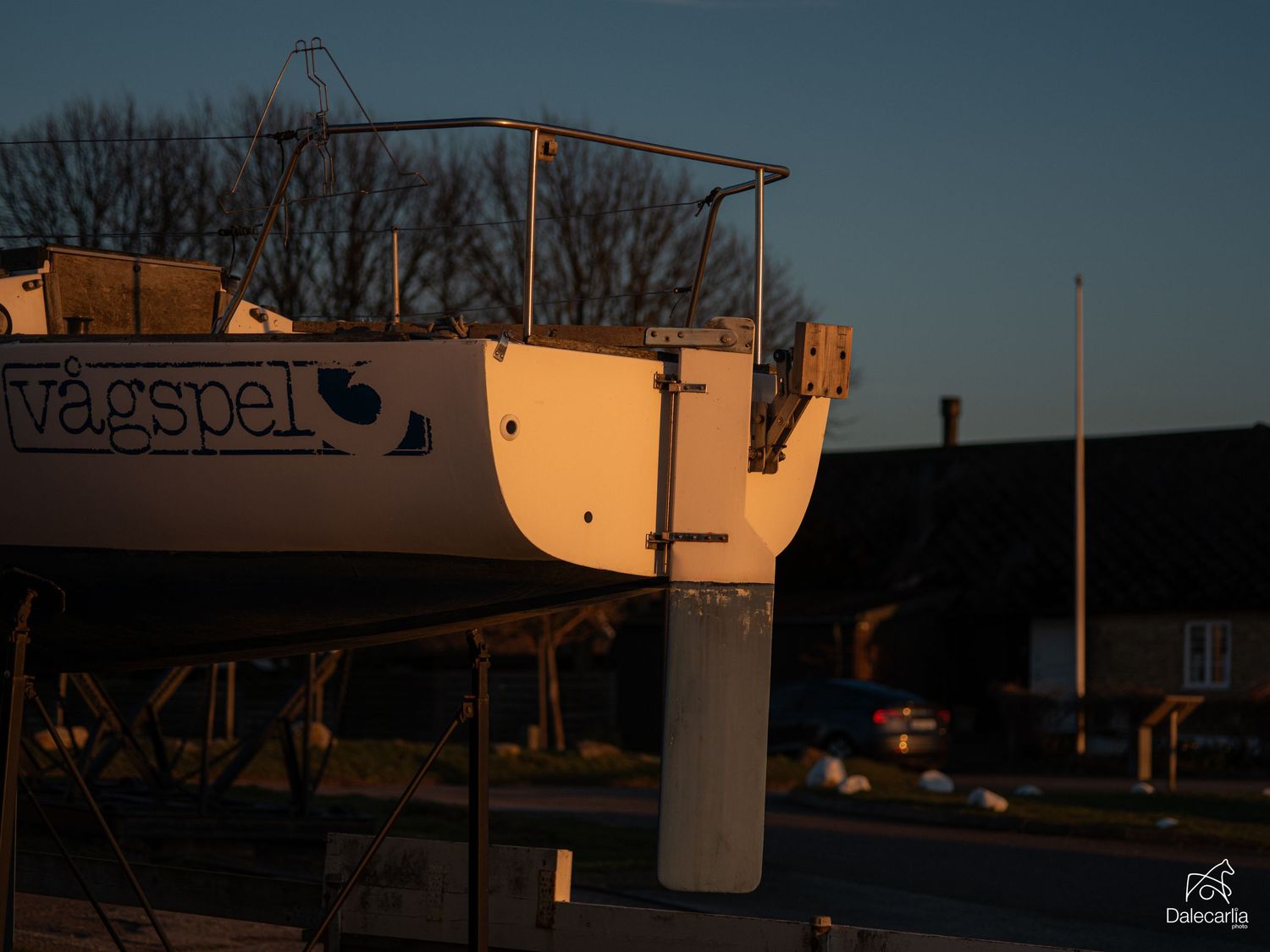 Sailboat named Vagspel stored on land at sunset in a marina yard.