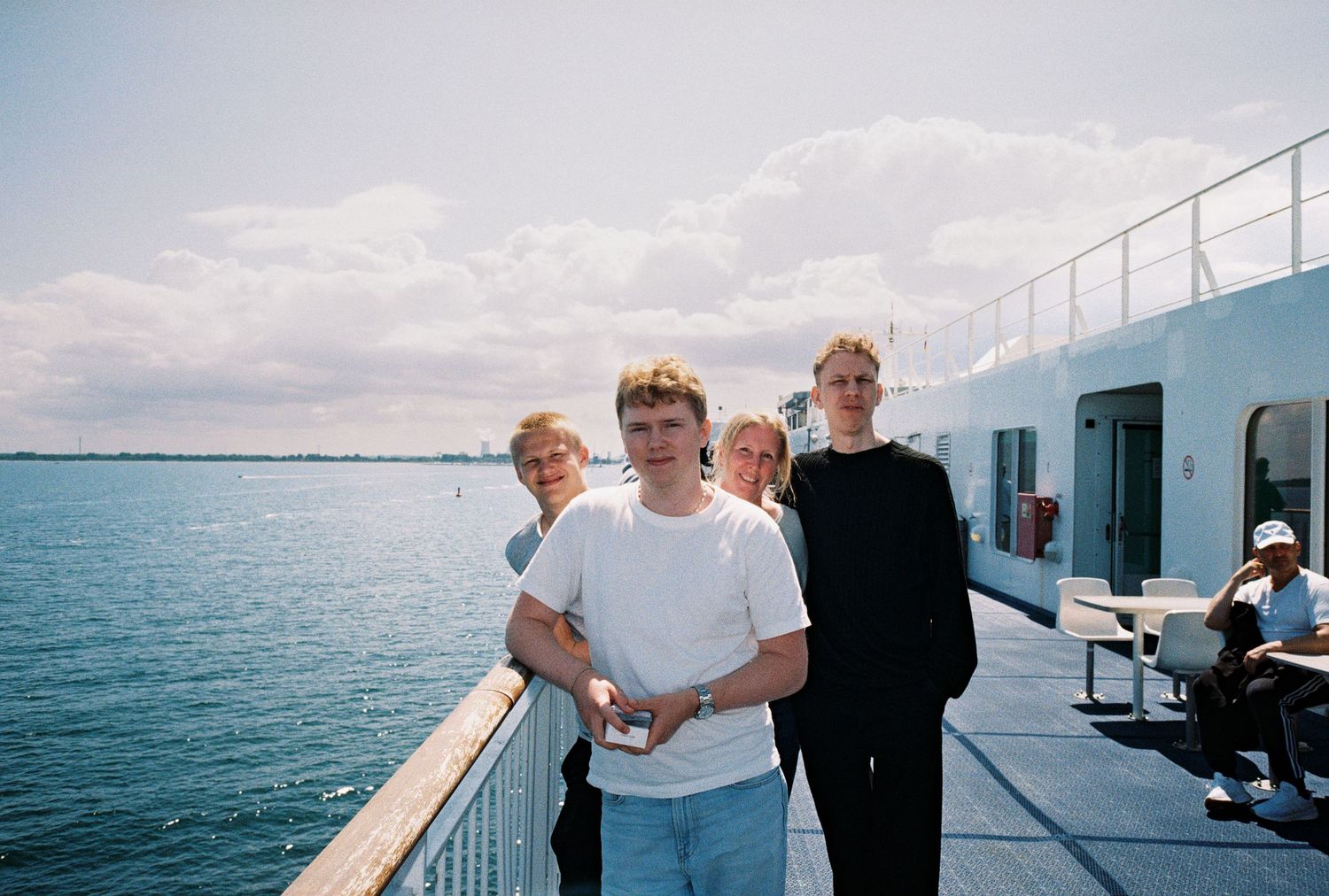 People standing on a boat deck with blue water and cloudy sky in the background.