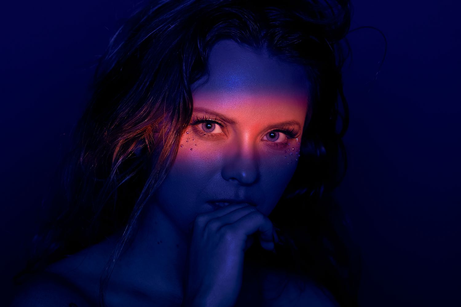 Moody portrait in dark blue lighting with subtle red highlights.