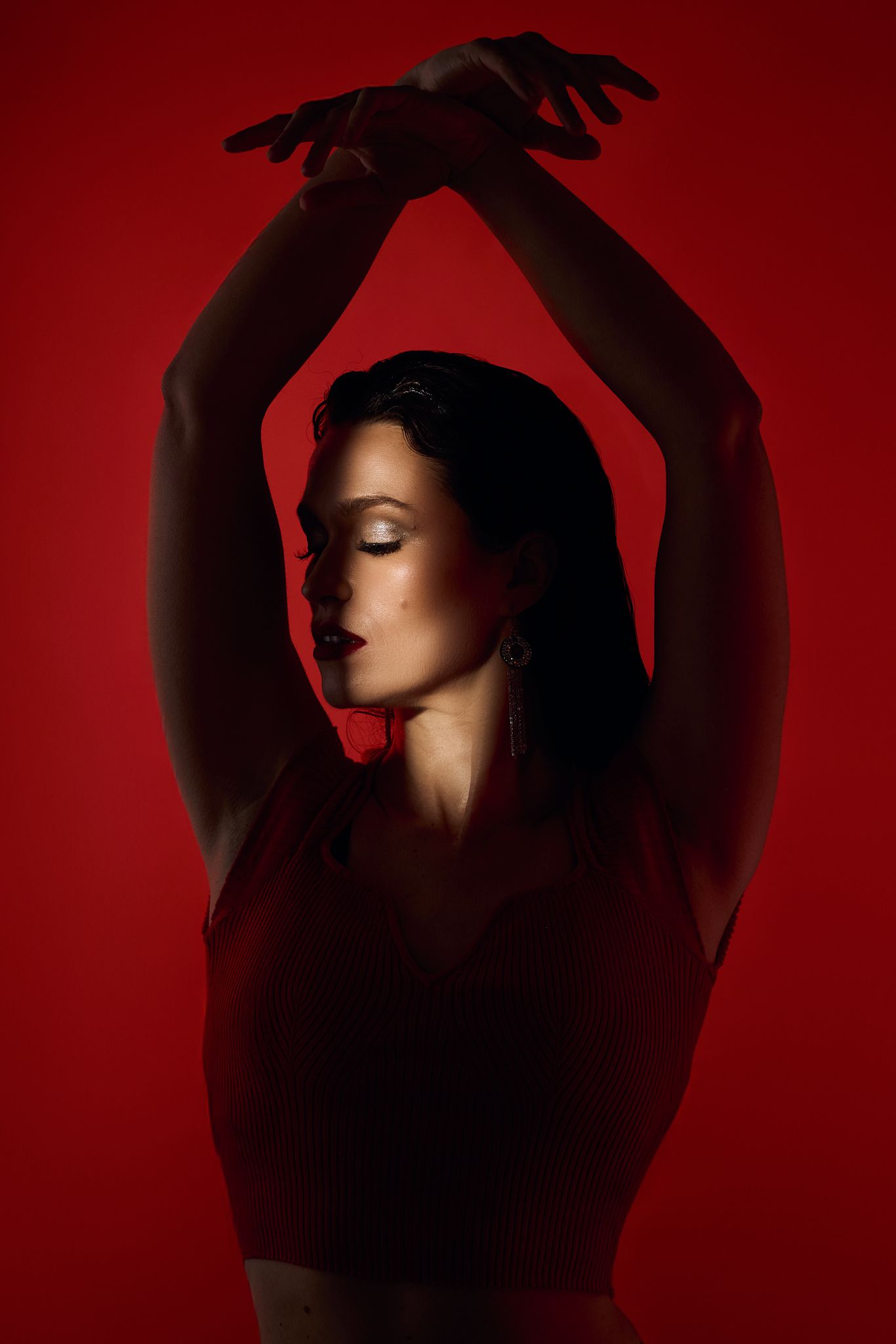 Artistic silhouette with raised arms against red background in dramatic lighting.