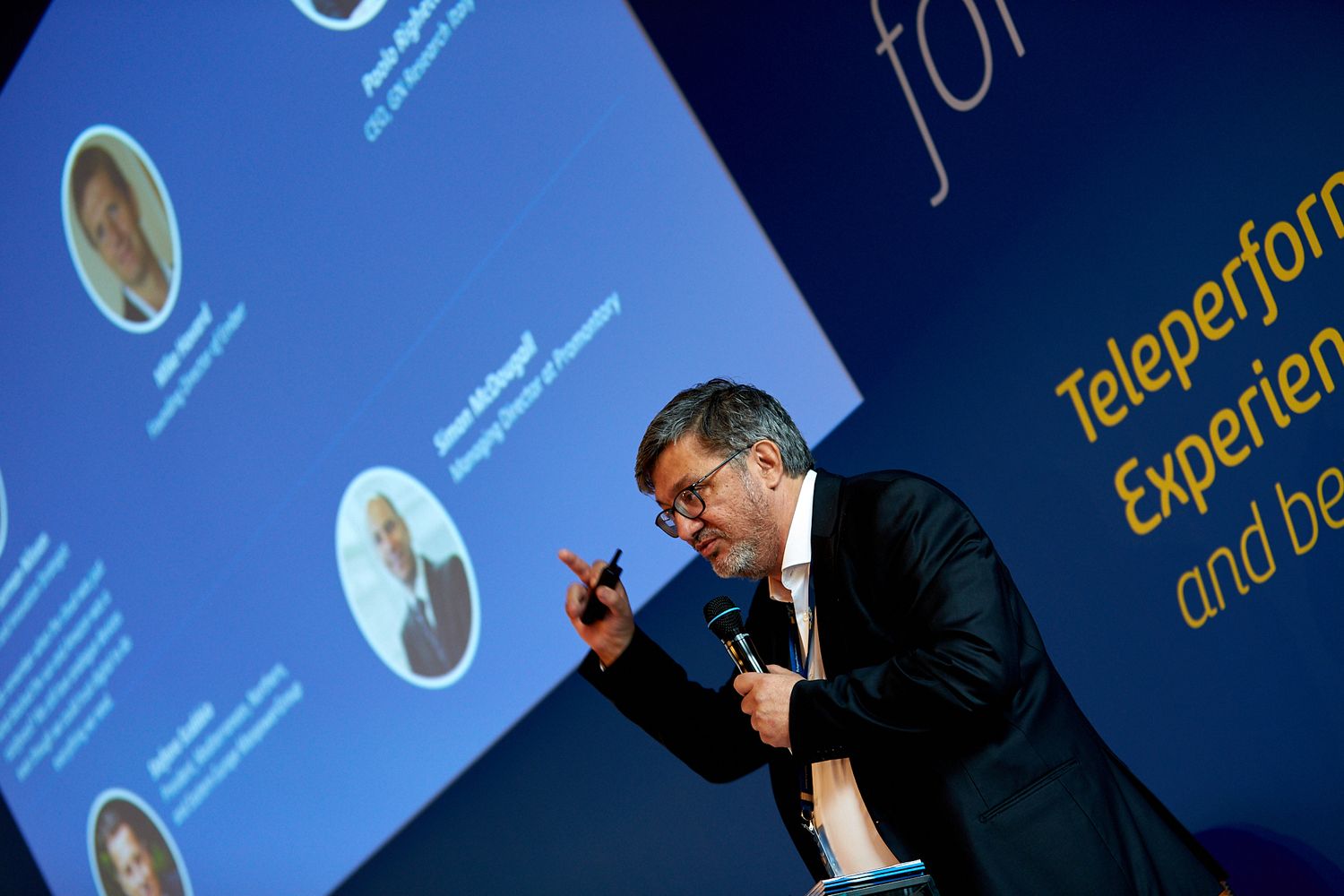 Professional conference presentation with blue projection screen and speaker profile.