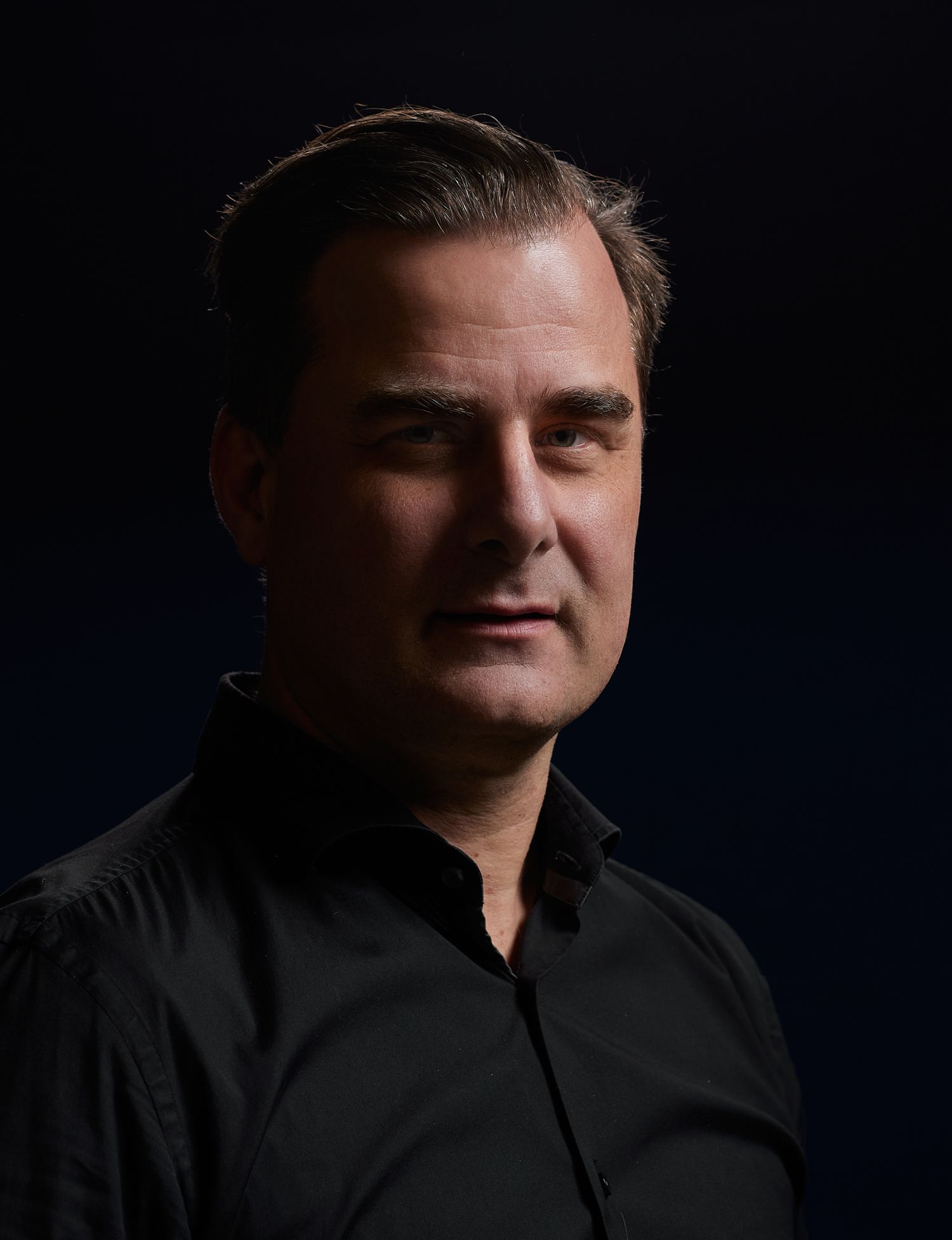 Professional headshots against dark background showing various poses in black attire.