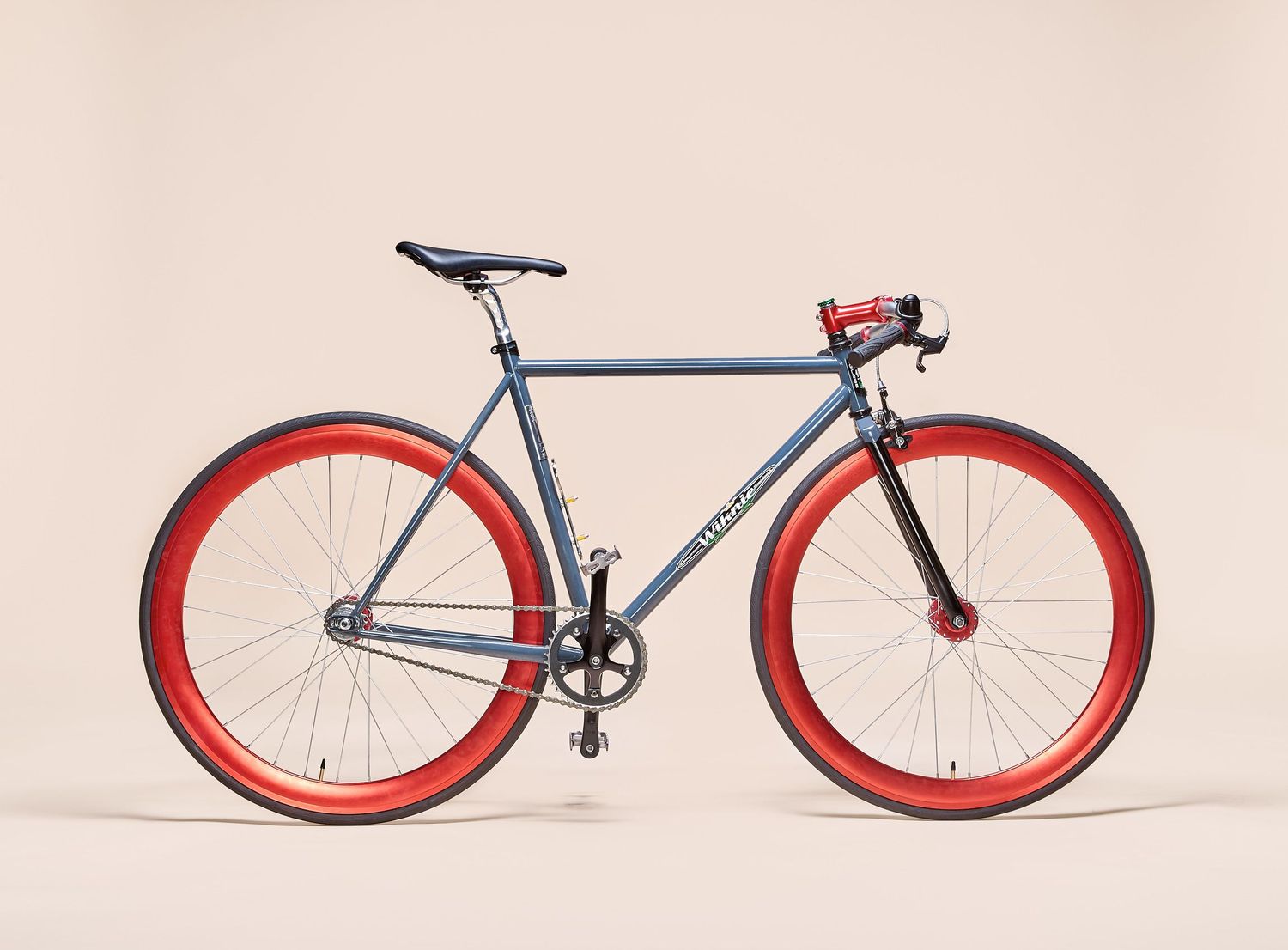 Minimalist fixed gear bicycle with red wheels and silver frame on beige background.