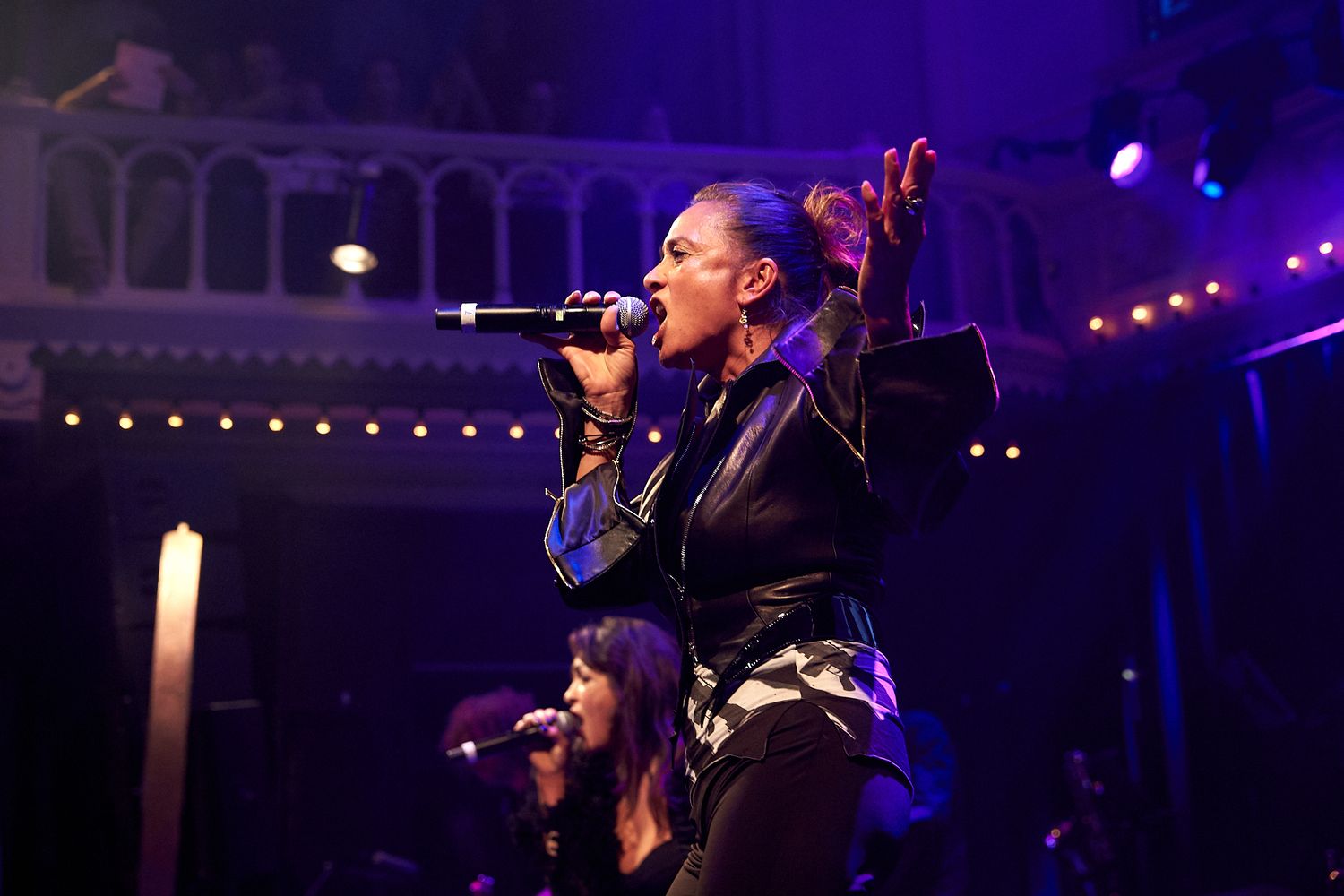 Concert performers on stage with purple lighting and theatrical effects.