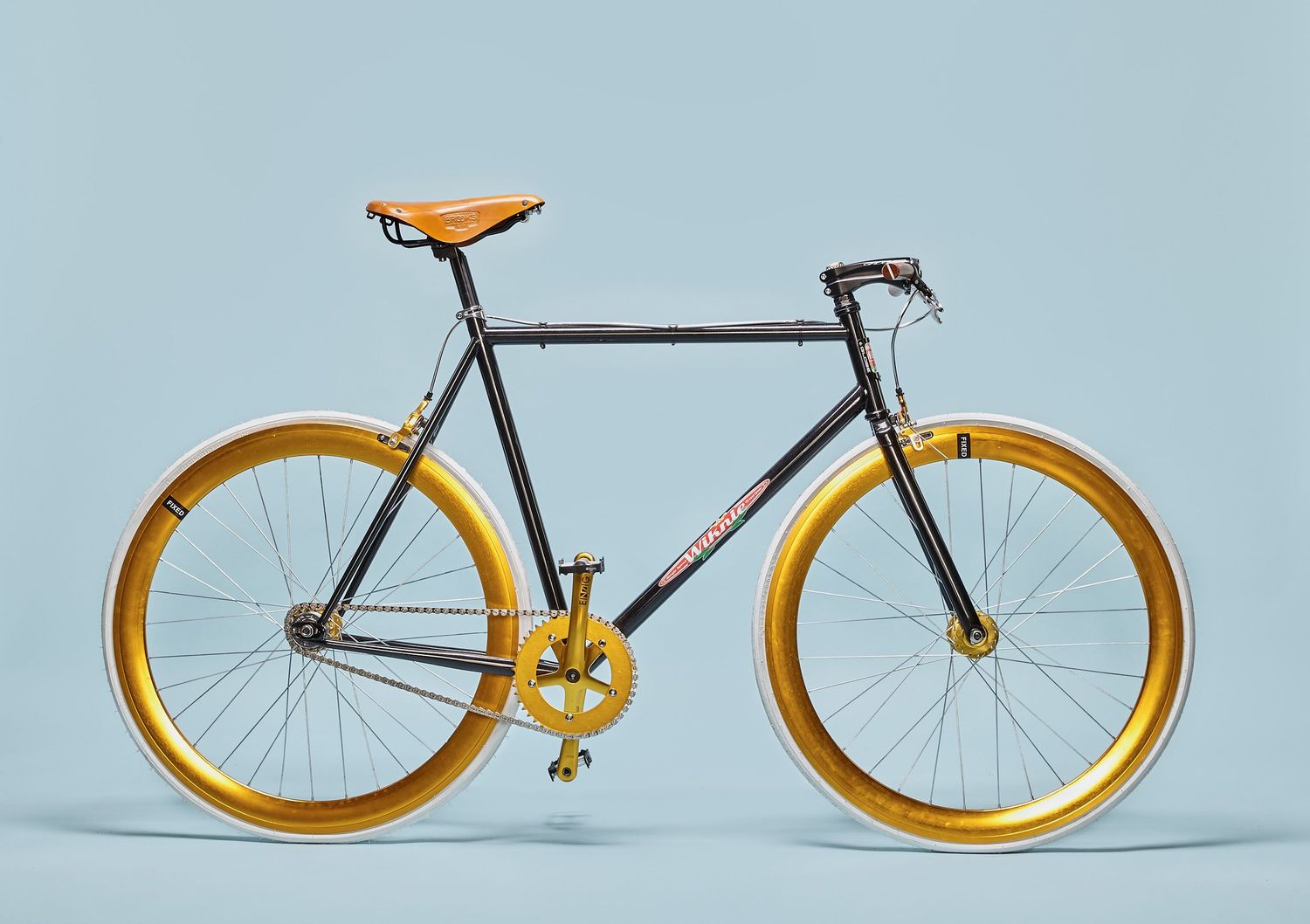Fixed gear bicycle with orange wheels and black frame photographed on light blue background.