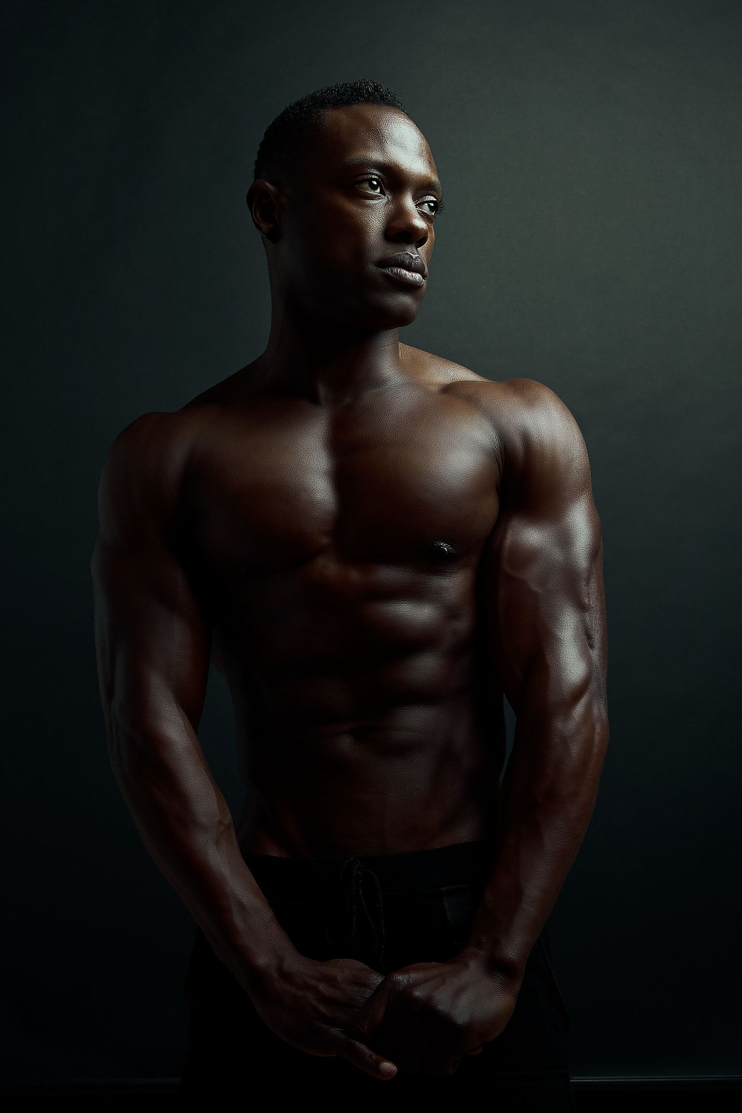 Artistic male fitness portrait showing muscular torso in dramatic low-key lighting.