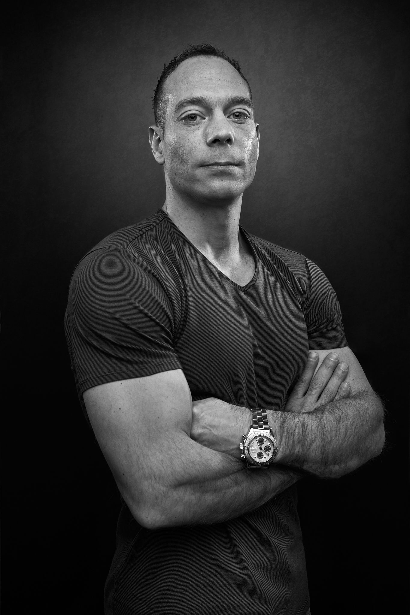 Black and white portrait series showing someone in a dark t-shirt with crossed arms against a dark background.
