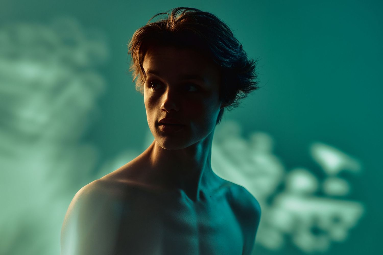 Dramatic close-up portrait in teal lighting showing silhouetted figure against atmospheric background.