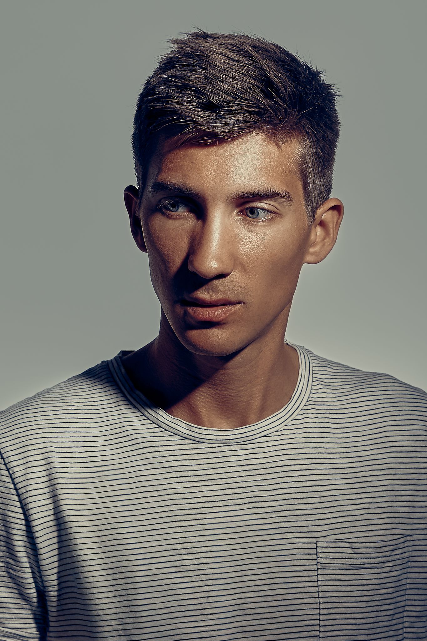 A series of moody studio portraits showing a person in a striped t-shirt against a gray background.