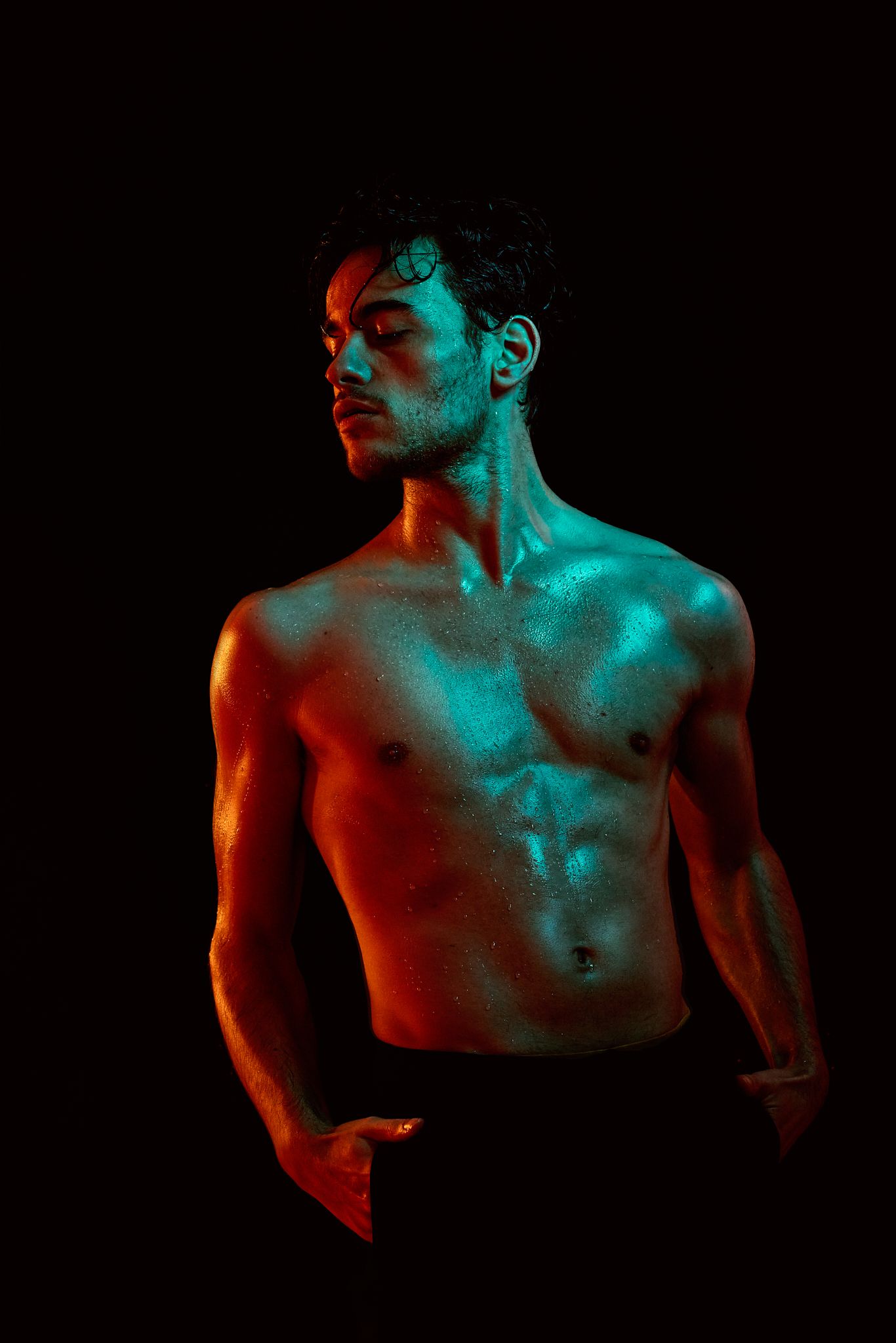 Dramatic portrait with red and turquoise lighting on shirtless muscular figure against black background.