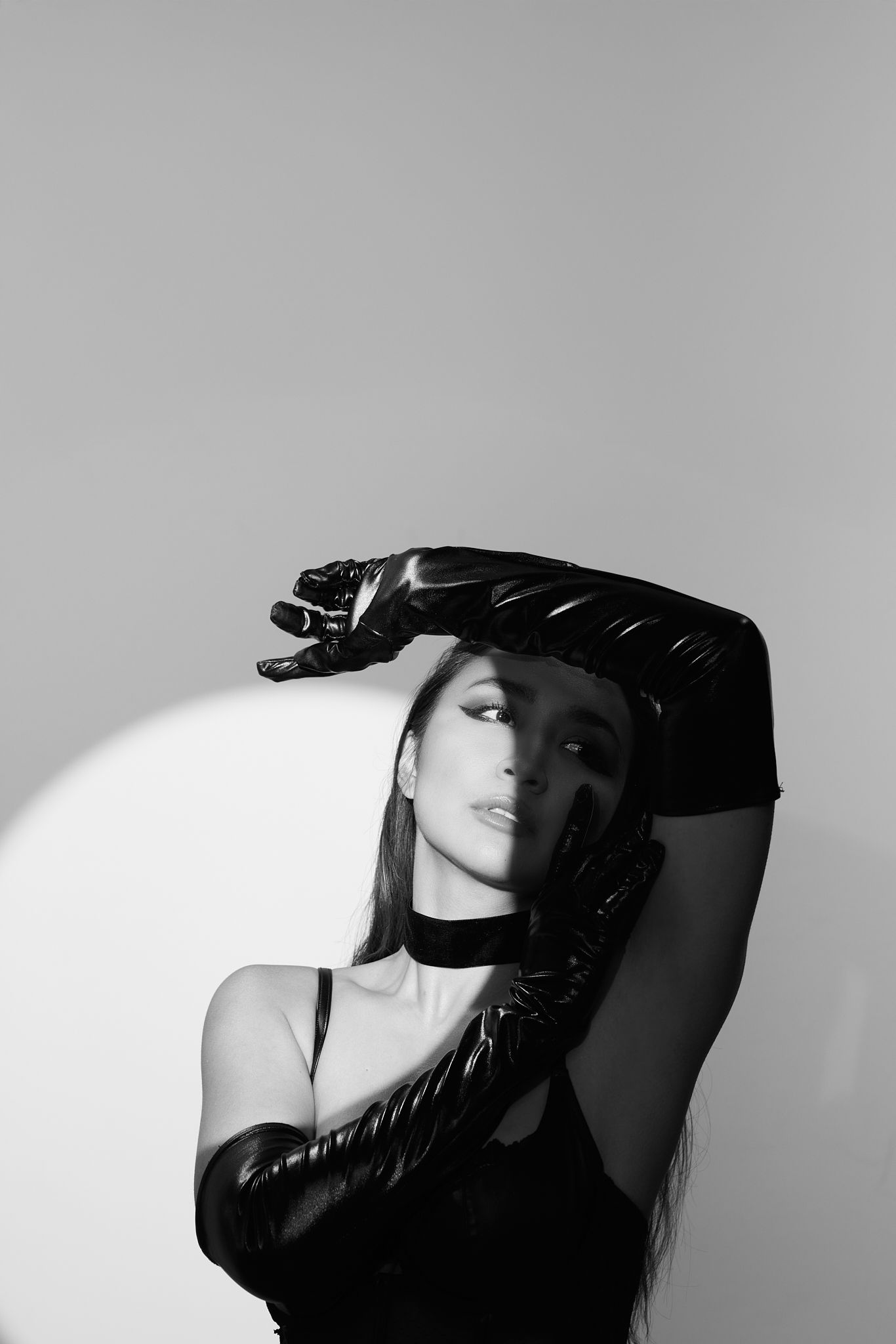 Artistic black and white photo of model in black outfit with dramatic arm pose.
