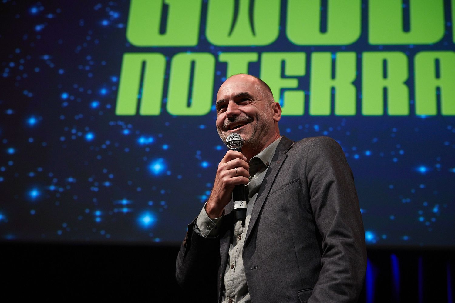 A stage presentation with bright green text displayed on a starry background screen.