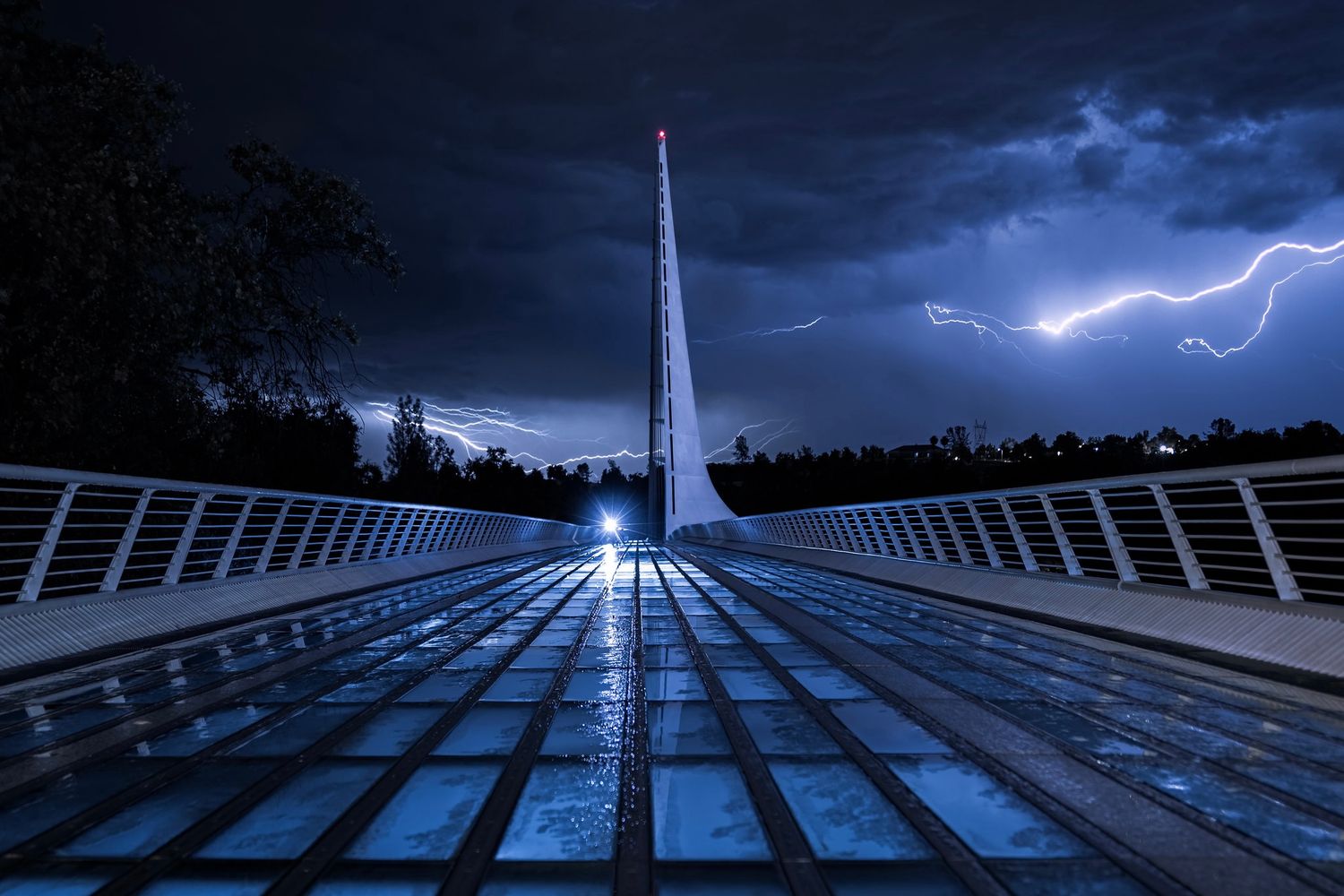 A photo of a dramatic lightning bolt illuminating a dark night sky over the Sundial Bridge on the Sacramento River in Redding, California.