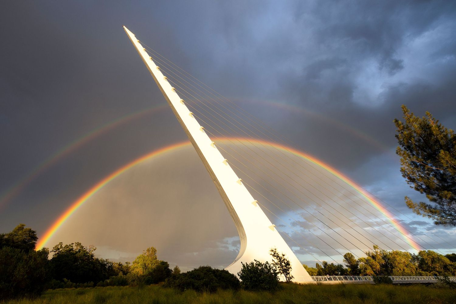 Double rainbow arching over the iconic Sundial Bridge in Redding, California, against a dramatic stormy sky.