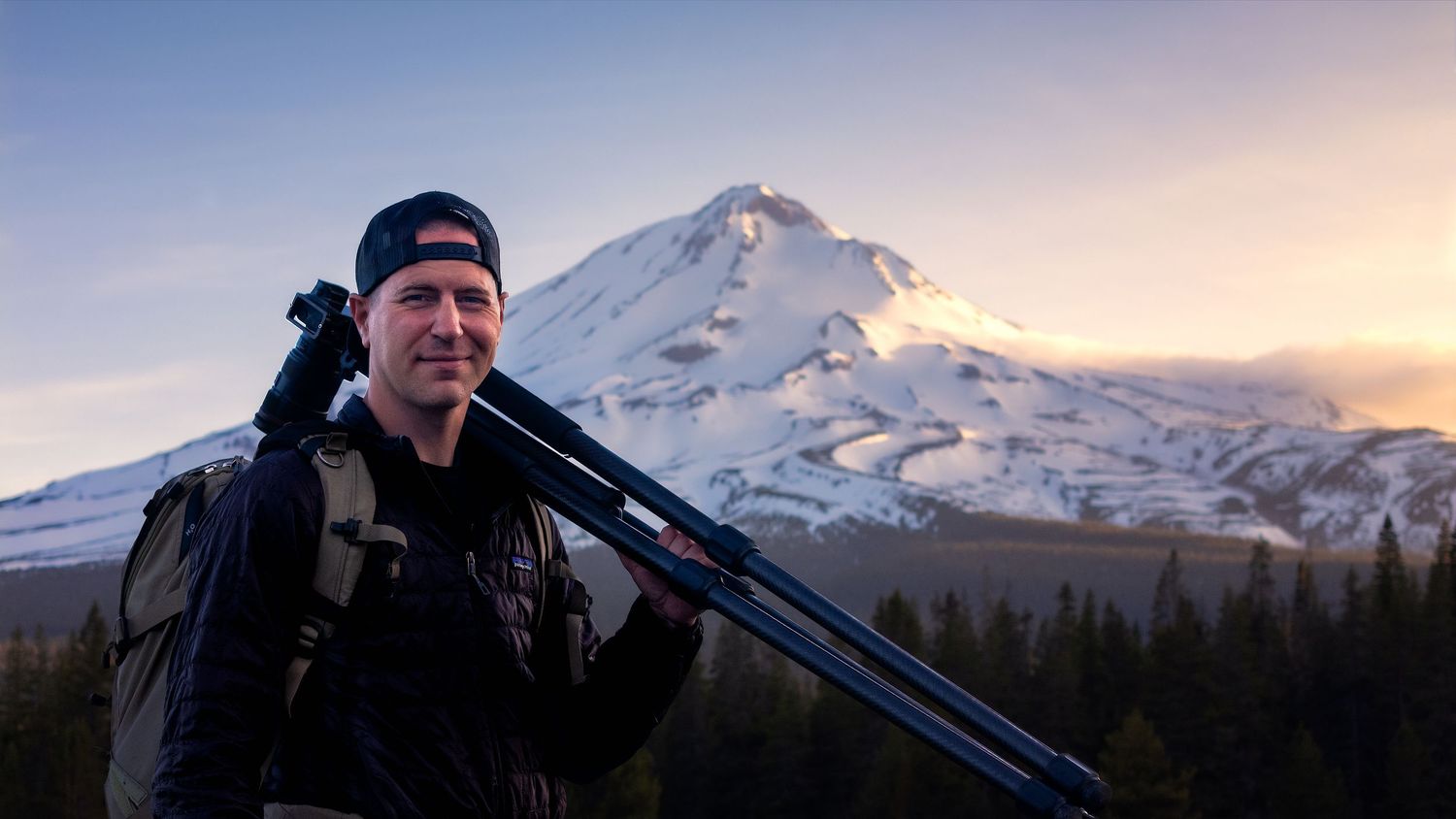 A shot of photographer Matt Haynie standing with his tripod before a scenic, snow-capped Mount Shasta forest and a golden sunset sky.