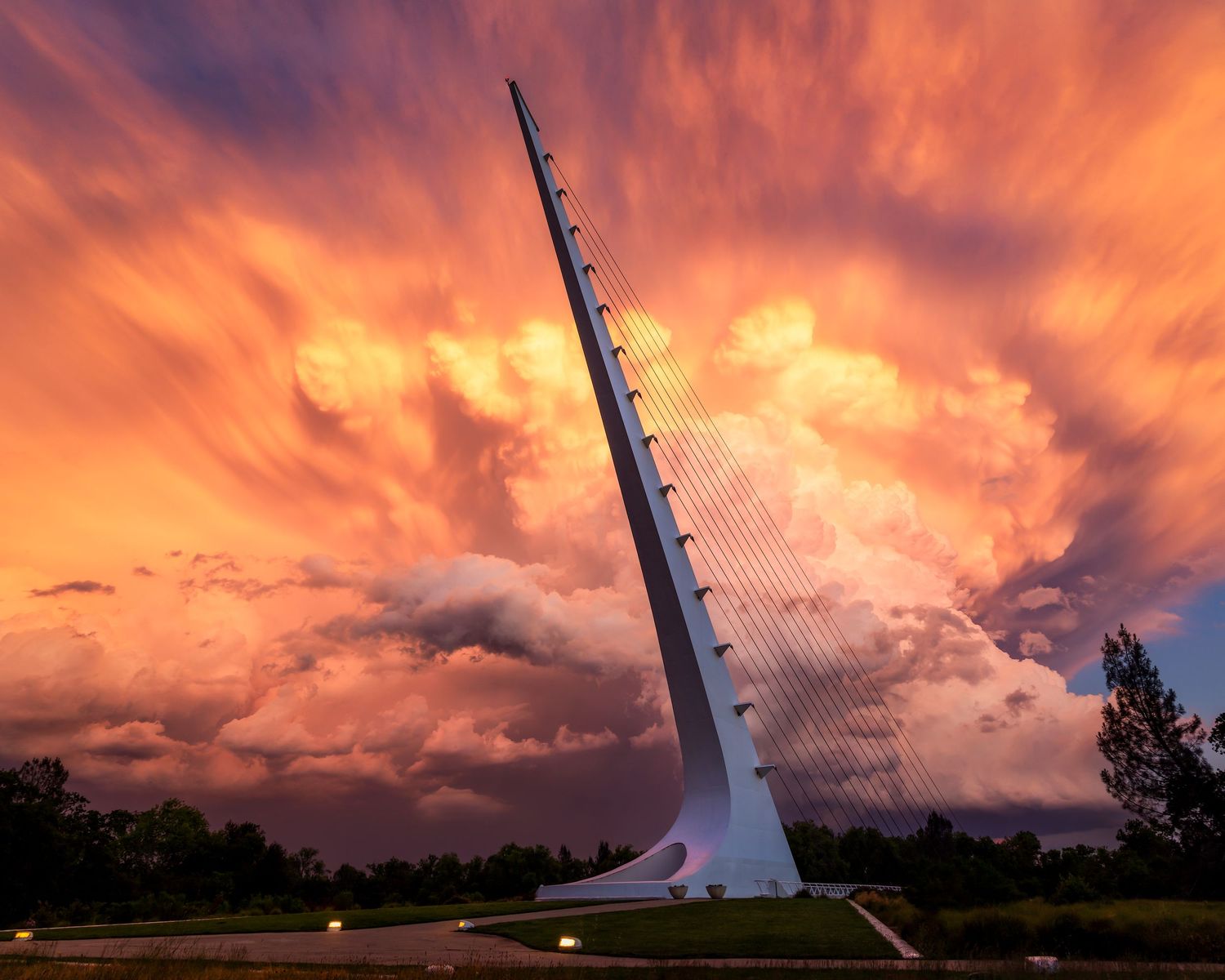 Sundial Bridge soars against a dramatic fiery orange sunset sky with billowing storm clouds in Redding, California.