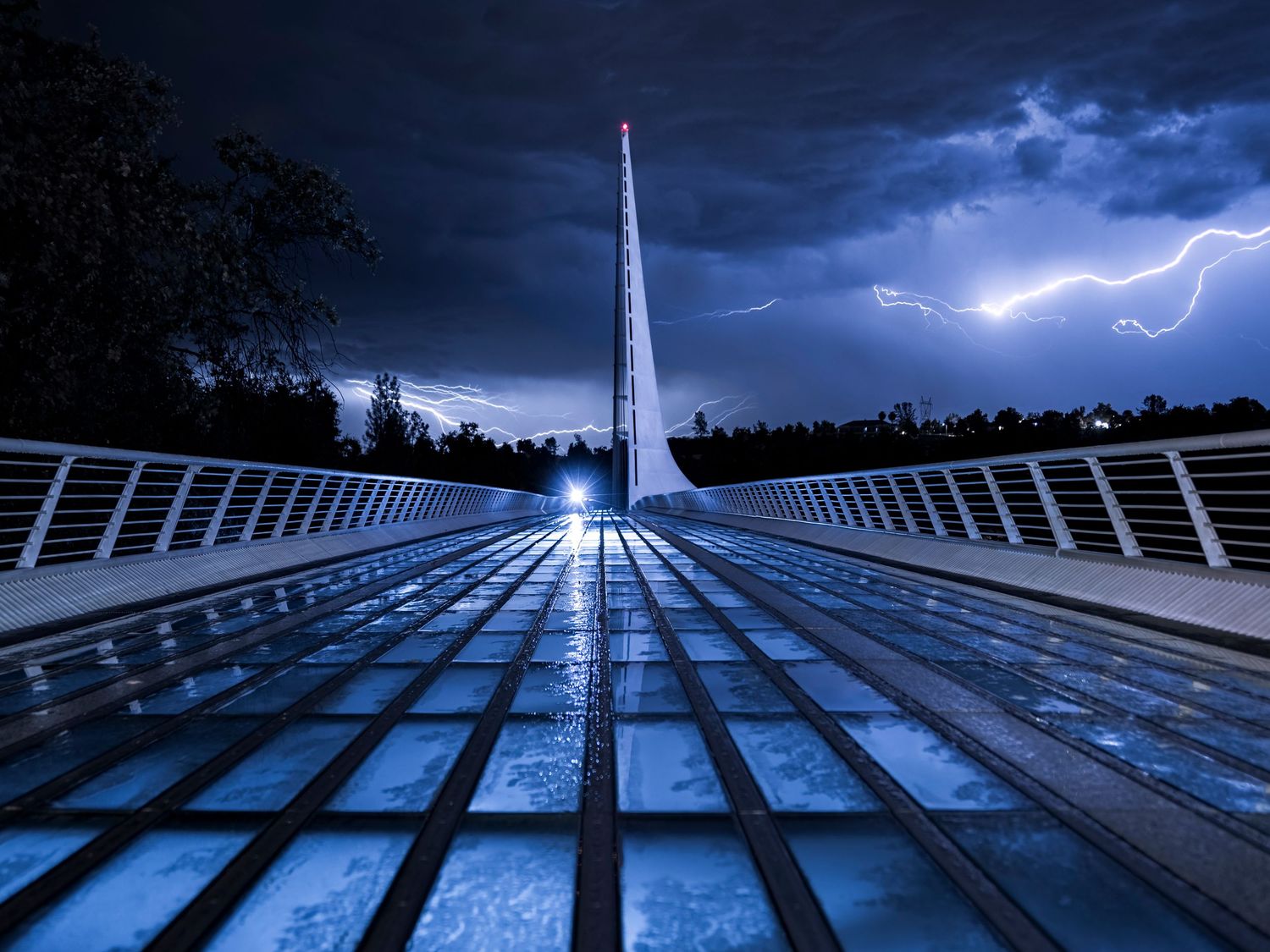 Sundial Bridge illuminated at night during a dramatic lightning storm with dark stormy skies in Redding, California.