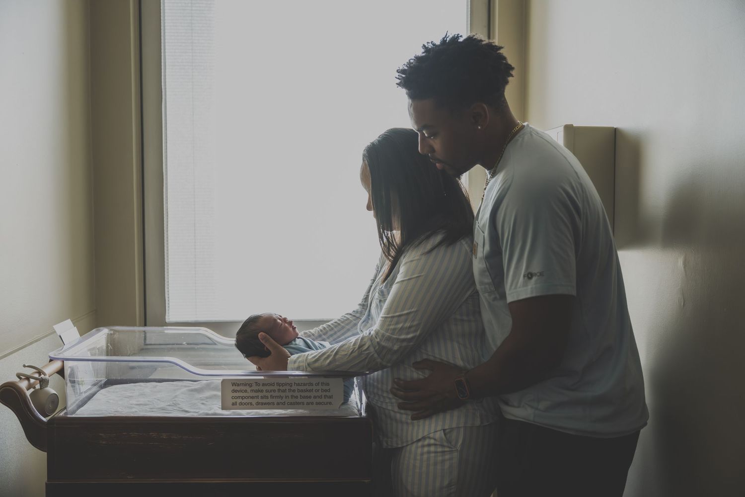 New parents standing together at a changing table, tenderly caring for their newborn baby by a bright window.