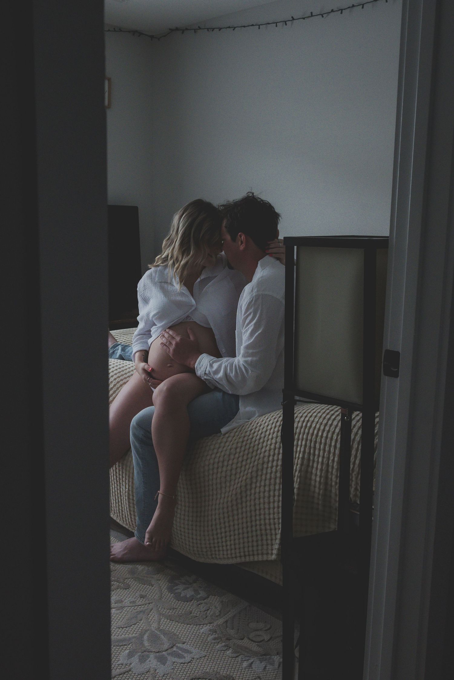 Intimate black and white boudoir maternity photography session showing soft lighting and delicate poses on a bed.