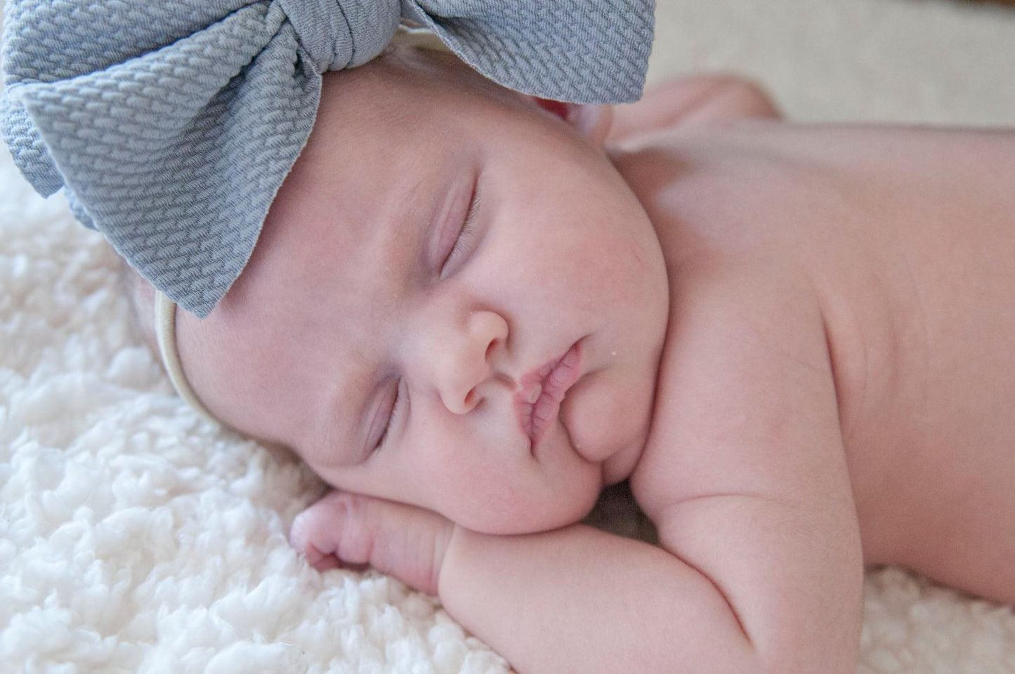 Peaceful sleeping newborn wearing a soft gray bow headband.