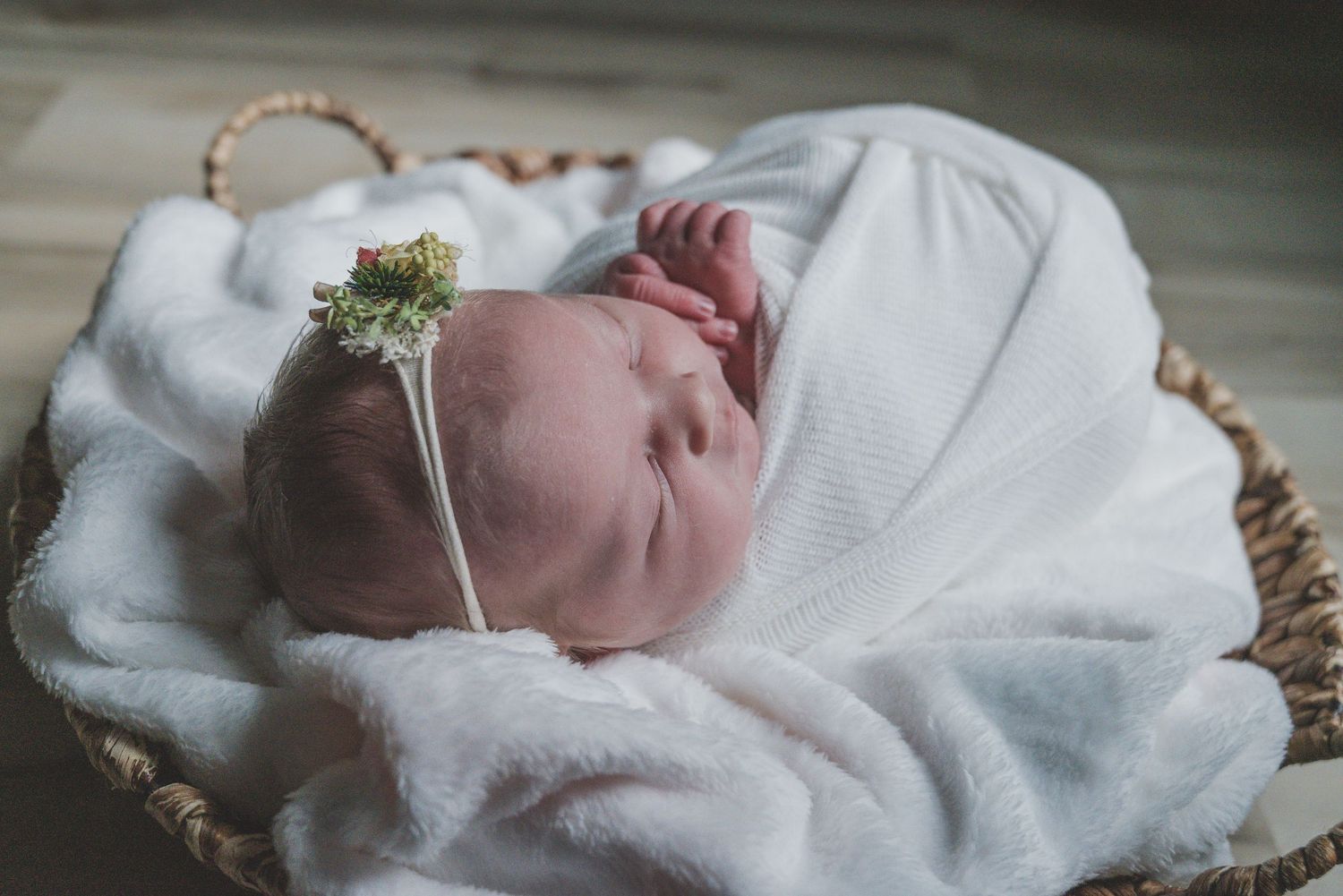 Sleeping newborn wrapped in white blanket during professional photography session.