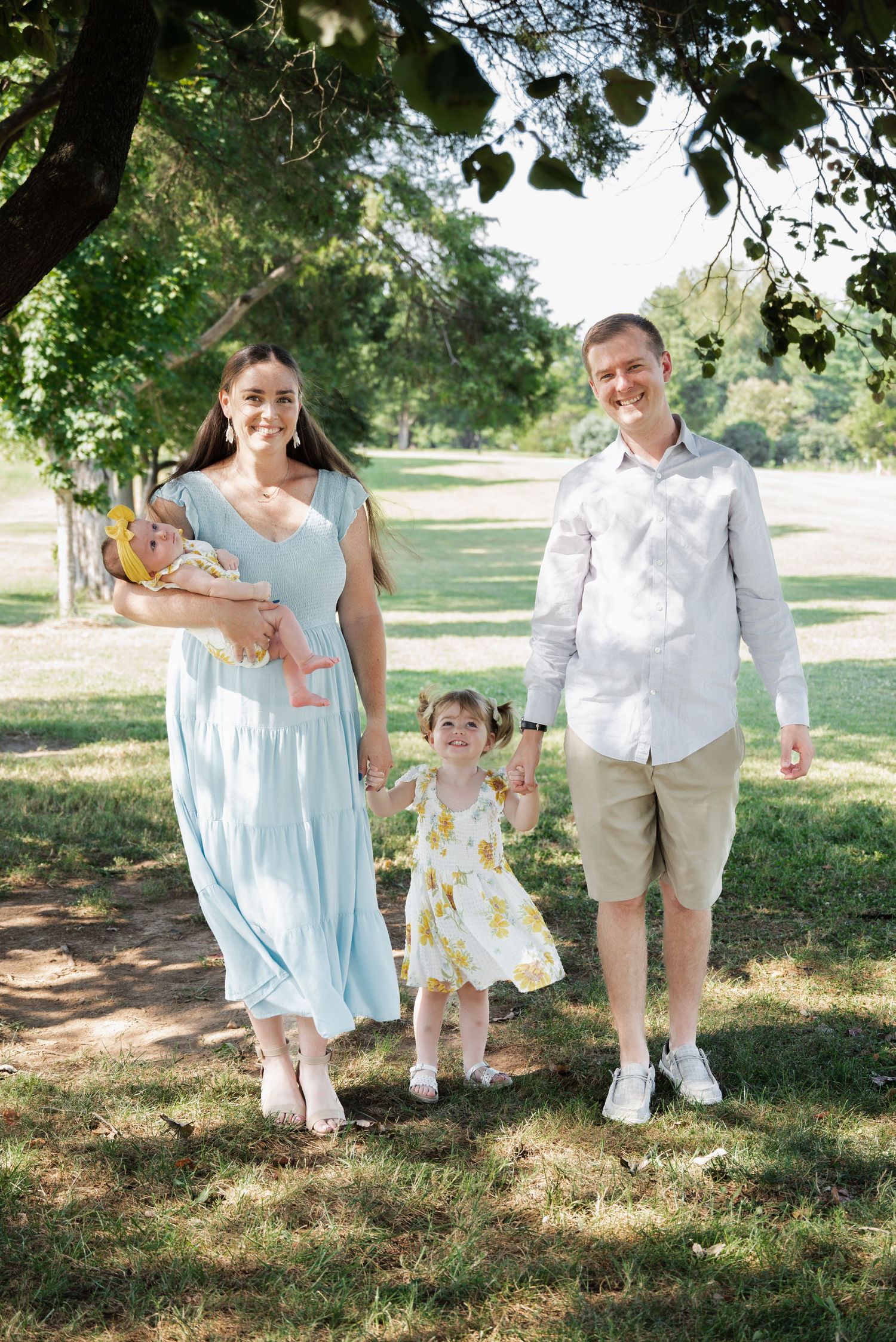 Family portrait session in a park with coordinated light blue and white summer outfits.
