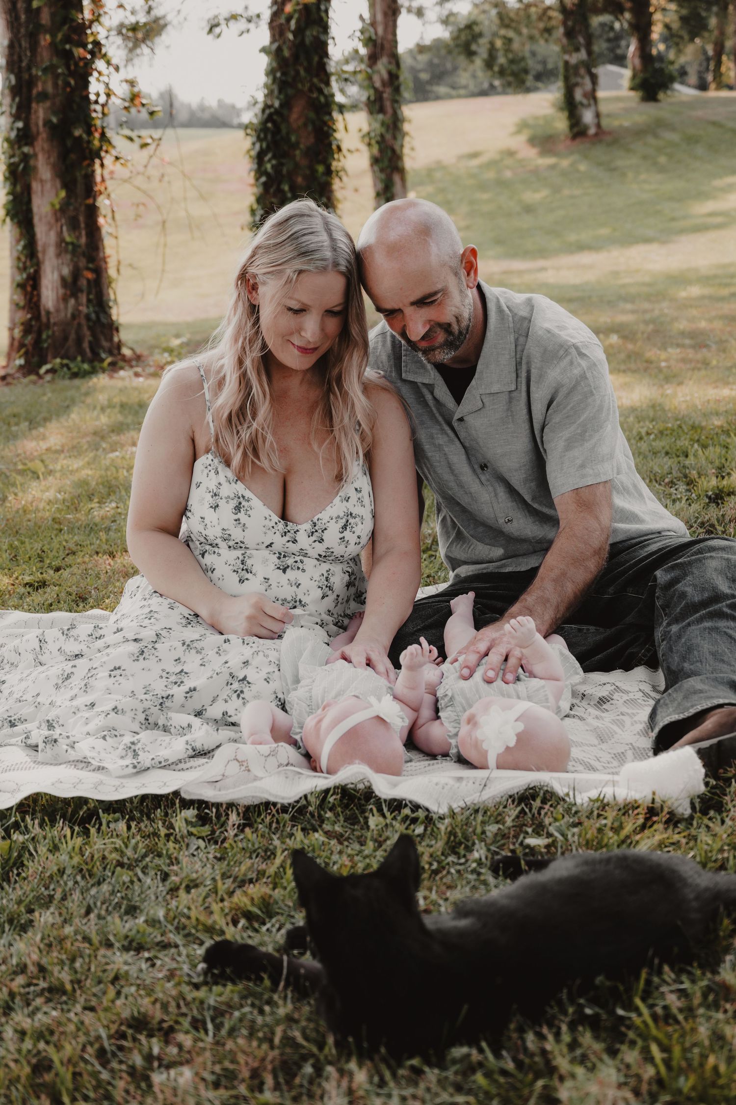Family photo session on grass with baby and black cat showing tender moments outdoors.