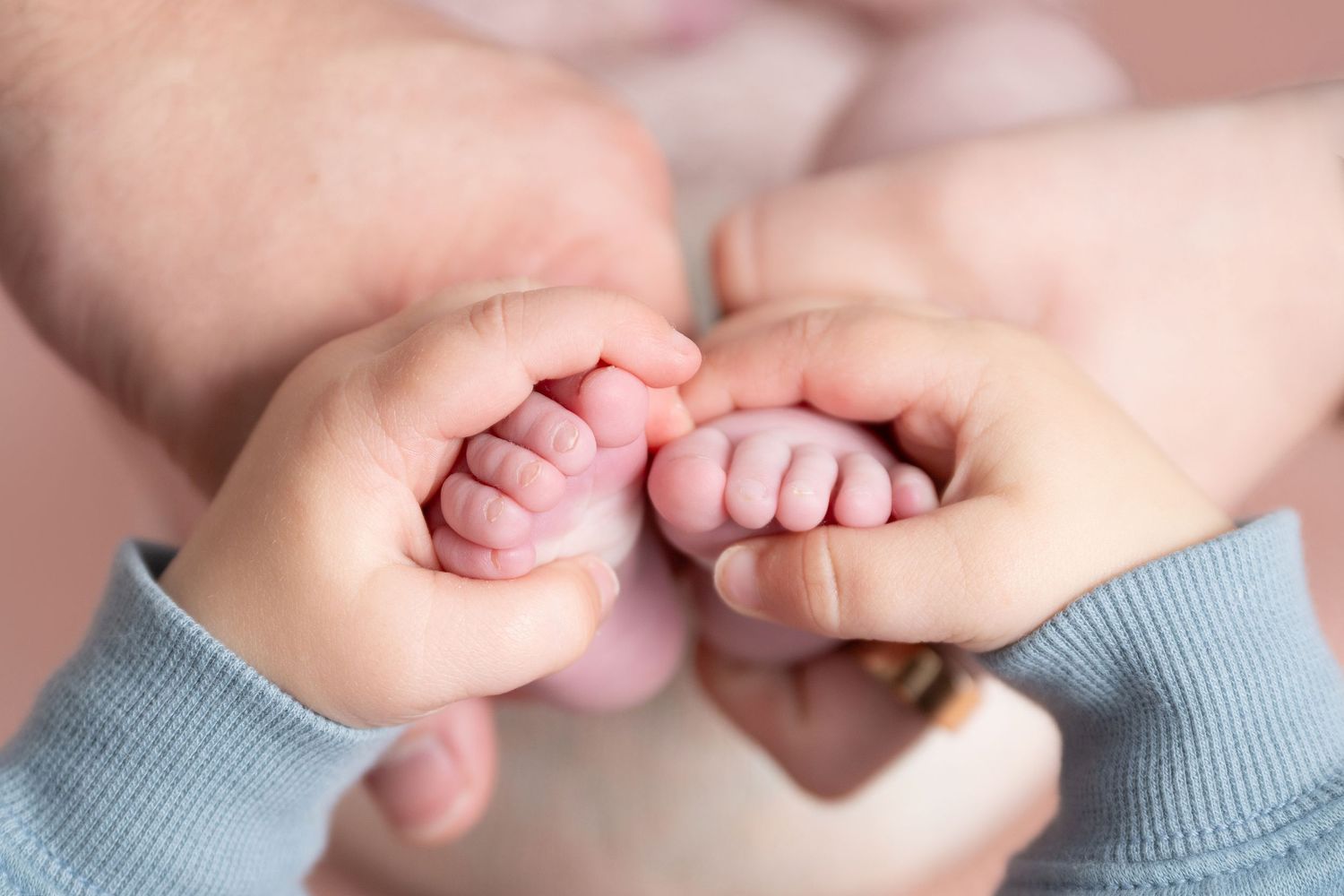 Adult hands gently holding tiny newborn baby feet and hands in a tender, close-up family bonding moment.
