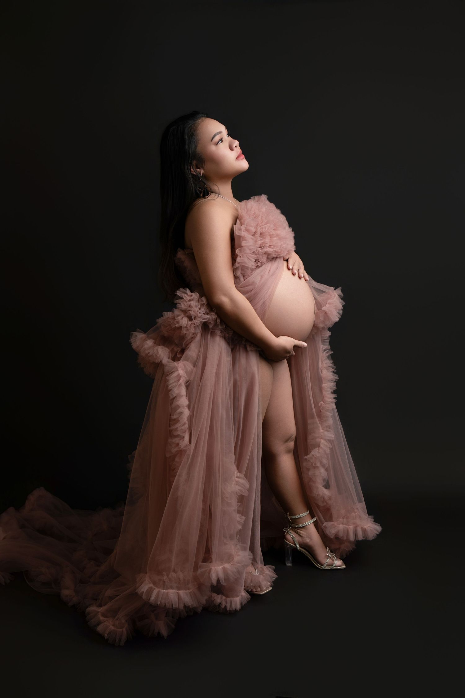 Artistic maternity portrait series showing a flowing dusty pink tulle gown against a dark background in four poses.